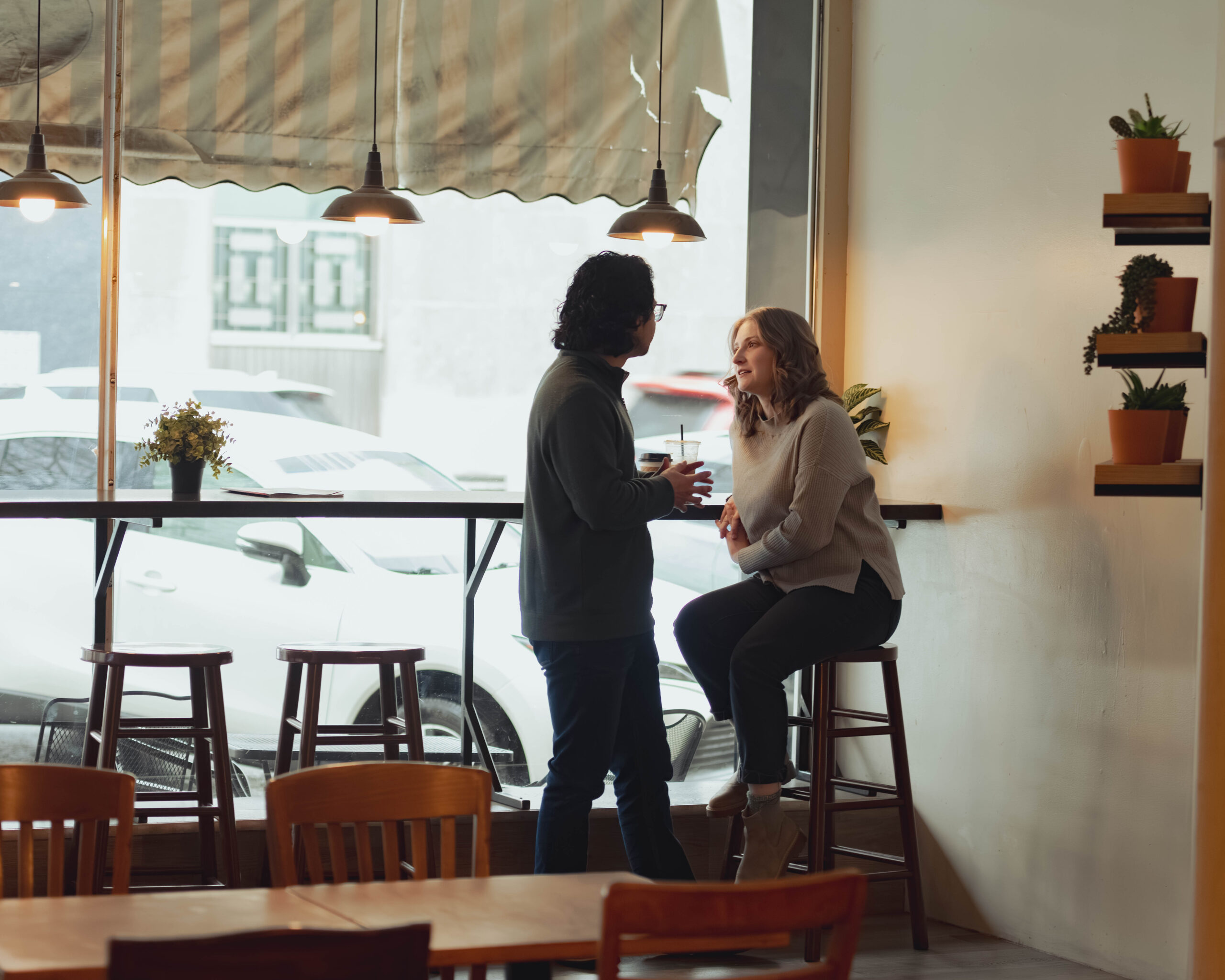 A man and woman sit on barstools at a coffee shop during their engagement session and talk to each other casually.