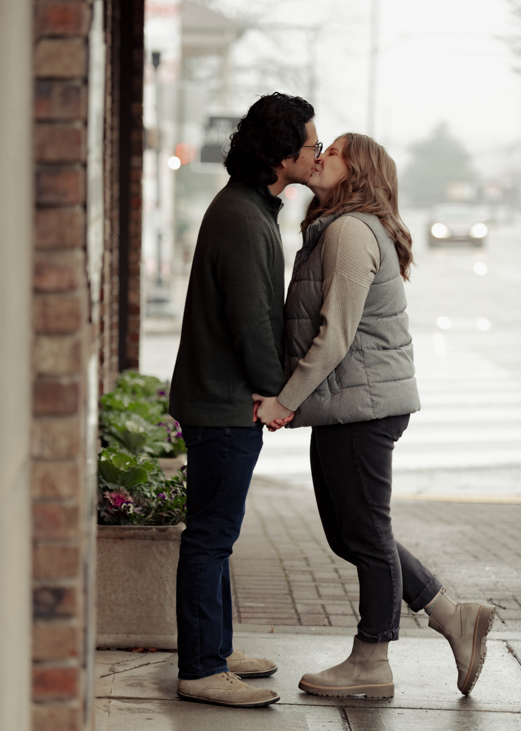 A man and woman kiss under an awning during their rainy engagement session.