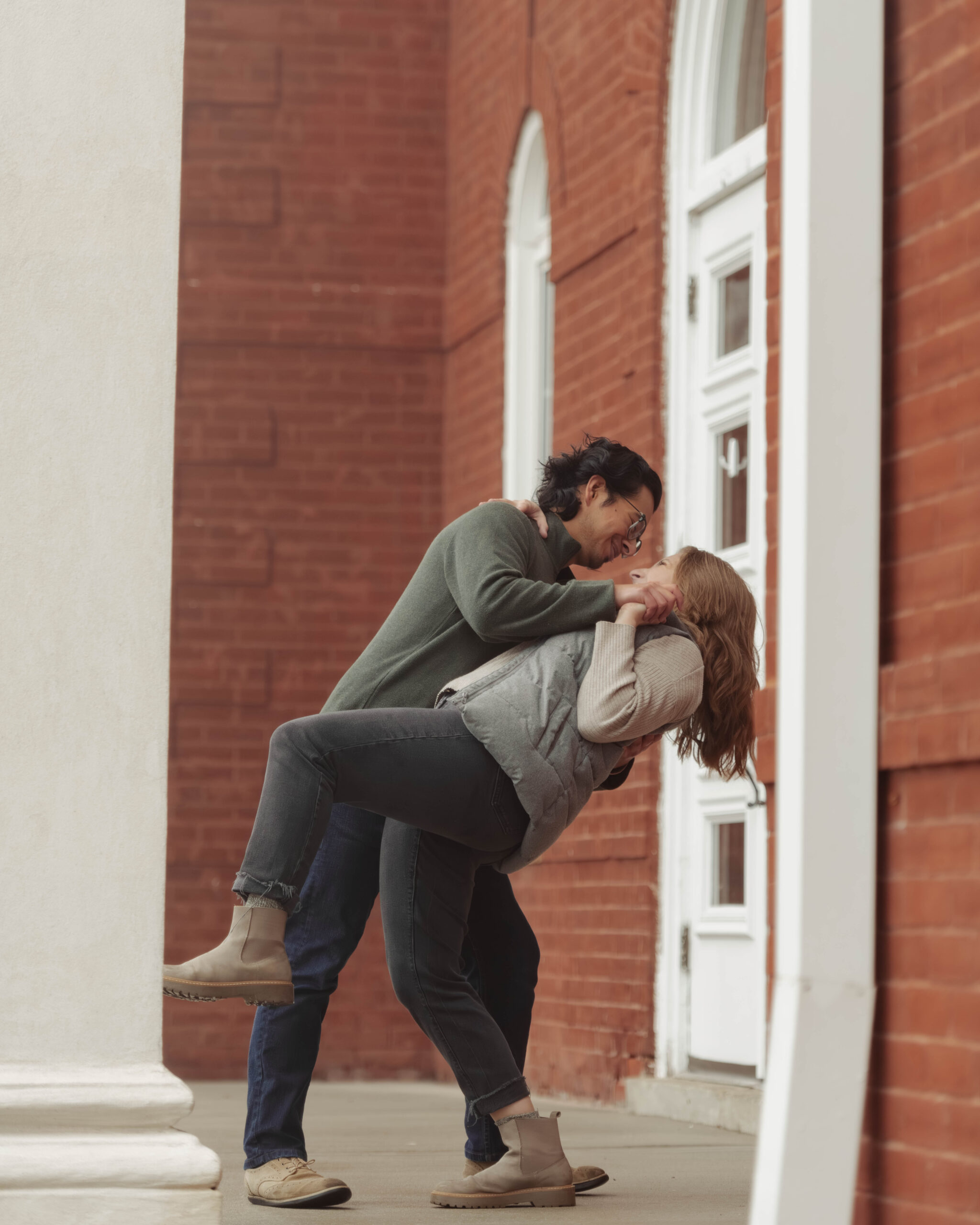 A man and woman dance on the steps of a courthouse during their engagement session. The man is dipping the woman backwards.