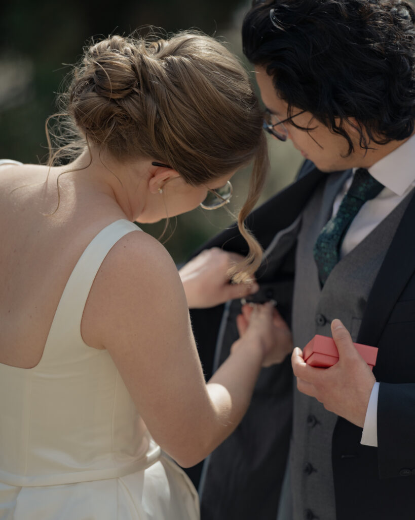 A bride helps a groom pin saint medals into his jacket before their wedding.