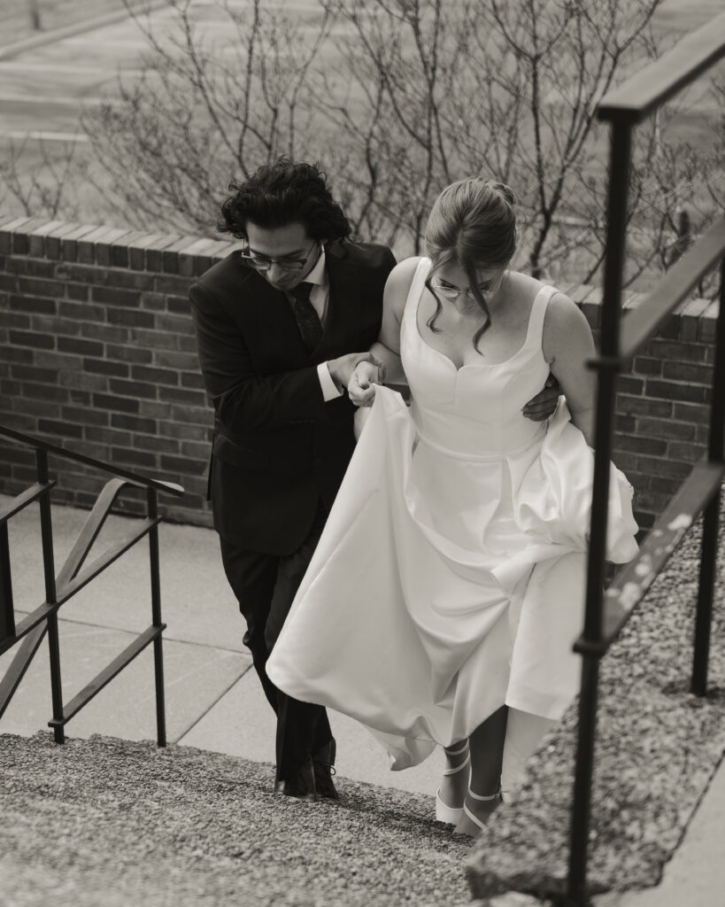 A groom helps a bride up some stairs, neither look at the camera.