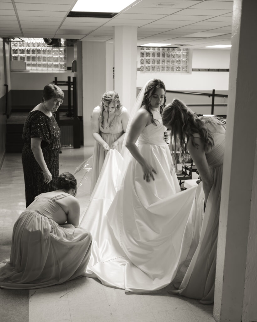 A bride her skirt cleaned and adjusted by her bridal party in the basement of the historic Our Lady of the Rosary Catholic church in downtown Dayton, Ohio.
