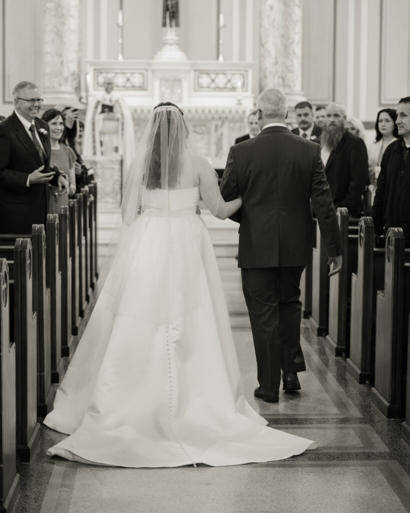 A catholic bride walks down the aisle with her father at a catholic wedding ceremony at Our Lady of the Rosary in Dayton, Ohio.