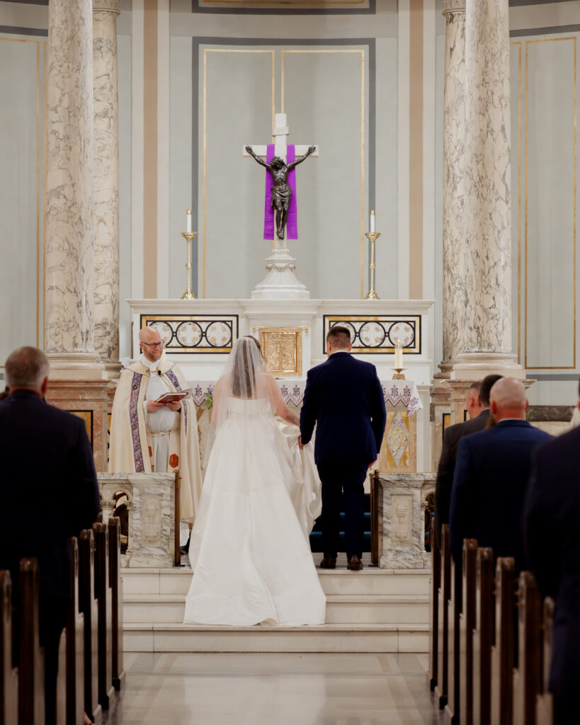 A bride and groom stand at the altar at their catholic wedding ceremony at Our Lady of the Rosary in Dayton, Ohio.