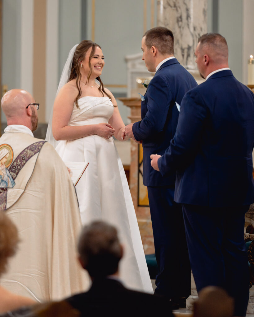 A catholic bride and groom exchange rings and smile during their catholic wedding ceremony at Our Lady of the Rosary in Dayton, Ohio.