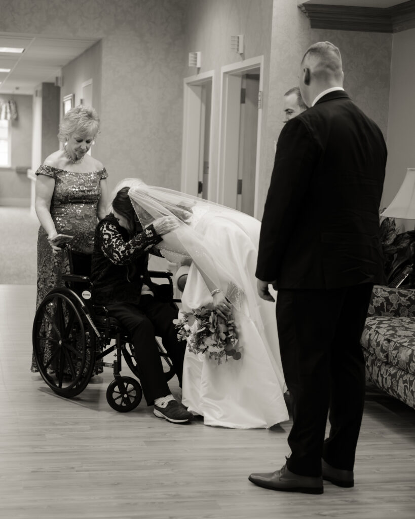 A catholic bride and groom visit with the grooms grandmother at a nursing home following their catholic wedding ceremony in Dayton, Ohio. The bride gives their grandmother a hug.