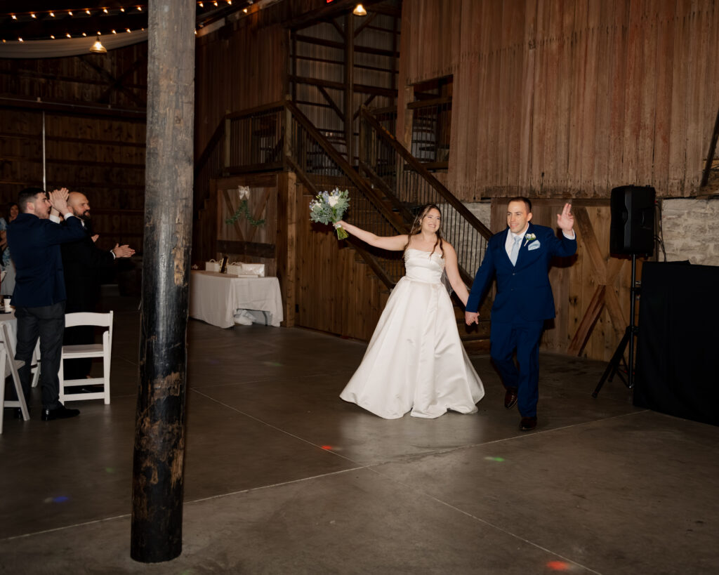 A catholic bride and groom enter their reception and wave.