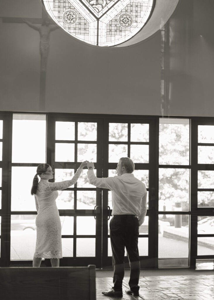 A catholic dances in the narthex of St. Mary's Catholic church in Jackson, Tennessee during their sunny engagement session ahead of their catholic wedding.