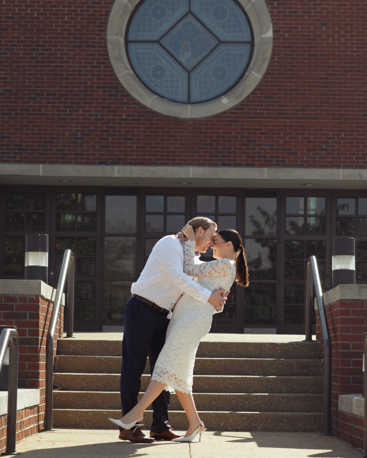 A catholic couple dances and laughs on the steps of St. Mary's Catholic church in Jackson, Tennessee during their sunny engagement session ahead of their catholic wedding.