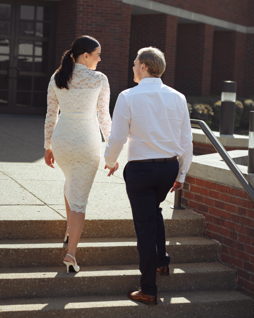 A catholic couple walks up the steps of St. Mary's Catholic church in Jackson, Tennessee during their sunny engagement session ahead of their catholic wedding.