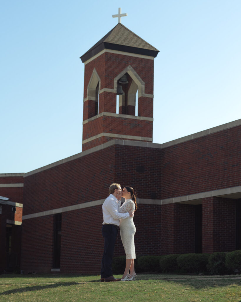A catholic couple kisses in front of St. Mary's Catholic church in Jackson, Tennessee during their sunny engagement session.