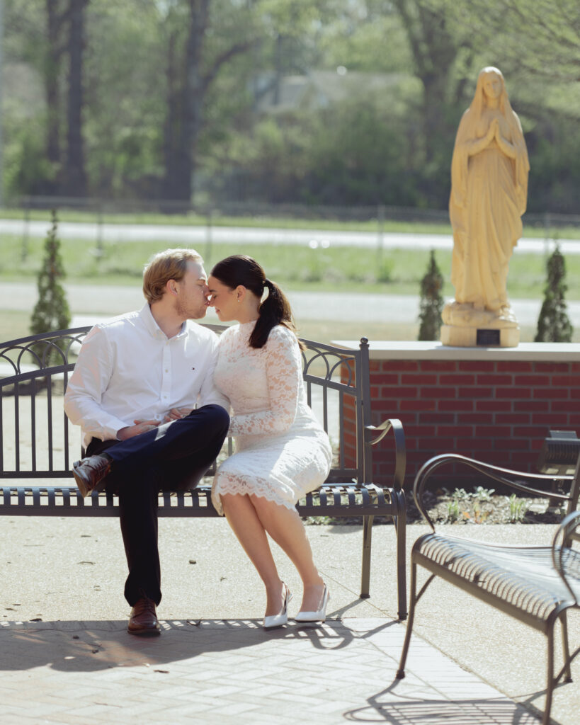 A catholic engaged couple pose in front of a statue of Mary at St. Mary's Catholic church in Jackson, Tennessee for their engagement session. The man kisses the woman on the forhead.
