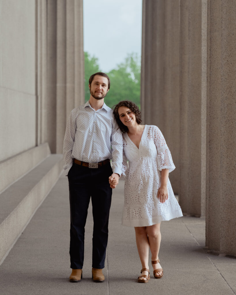 A catholic bride and groom lean into each other and look at the camera smiling during their nashville catholic engagement session at centennial park