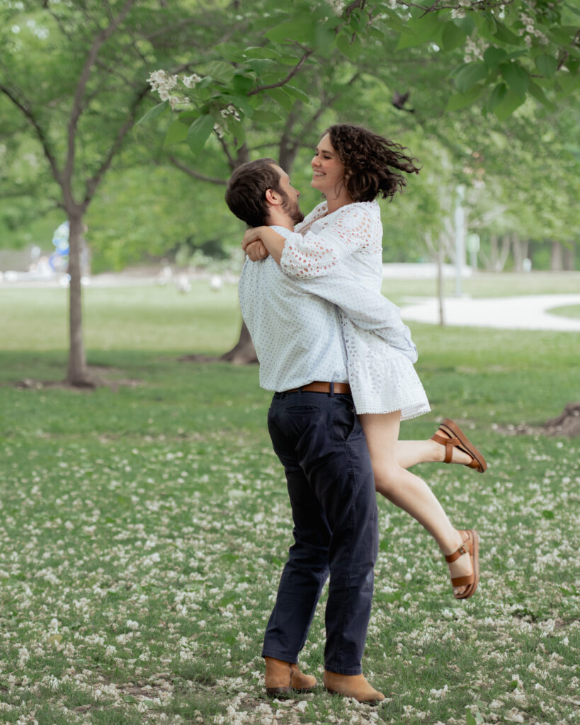 A catholic groom picks up his catholic bride and twirls her around during their catholic engagement session at centennial park in nashville, Tn