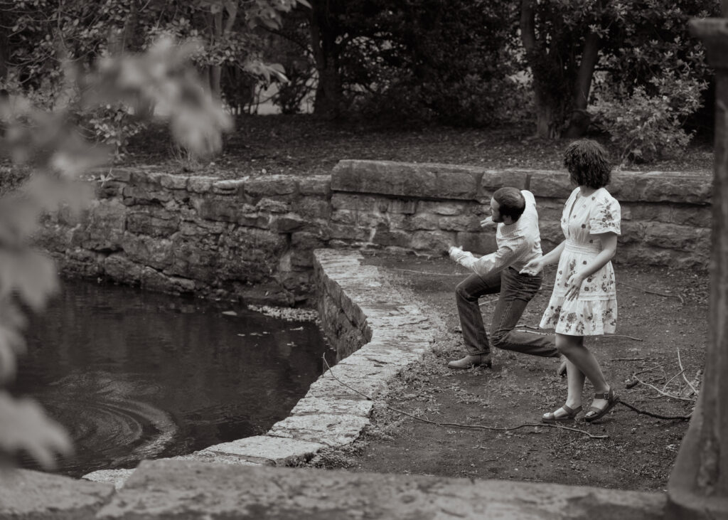 A catholic bride and groom skip rocks during their catholic engagement session at centennial park in nashville tennessee