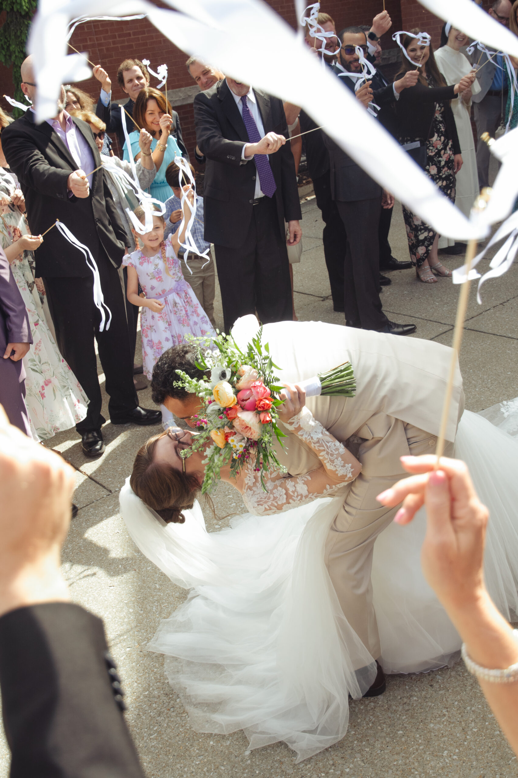 A catholic bride and groom share a dip kiss during their traditional church exit outside of holy family catholic church in brentwood, tennessee