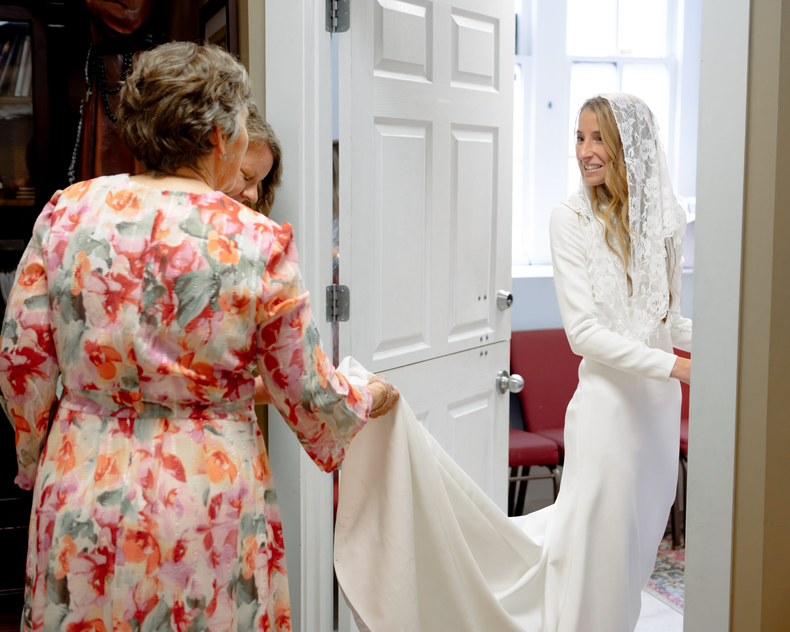 A catholic bride wearing a traditional catholic veil smiles her sister and mother at St. Mary's of the Seven Sorrows in downtown Nashville ahead of her catholic wedding Mass.