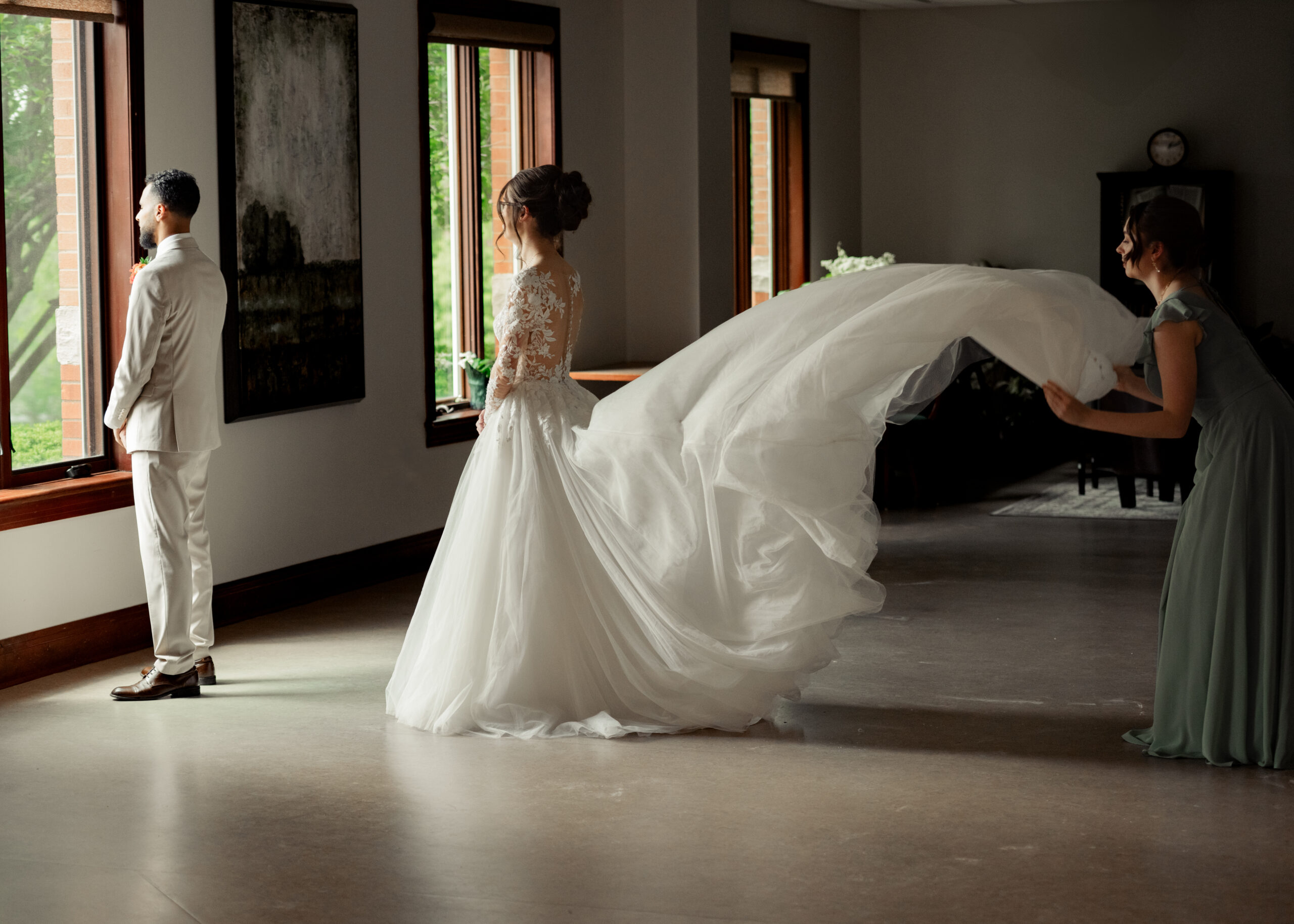 A bridesmaid fluffs the bride's dress as she prepares to turn her groom around for their first look at Holy Family catholic church in Nashville ahead of their catholic wedding Mass.