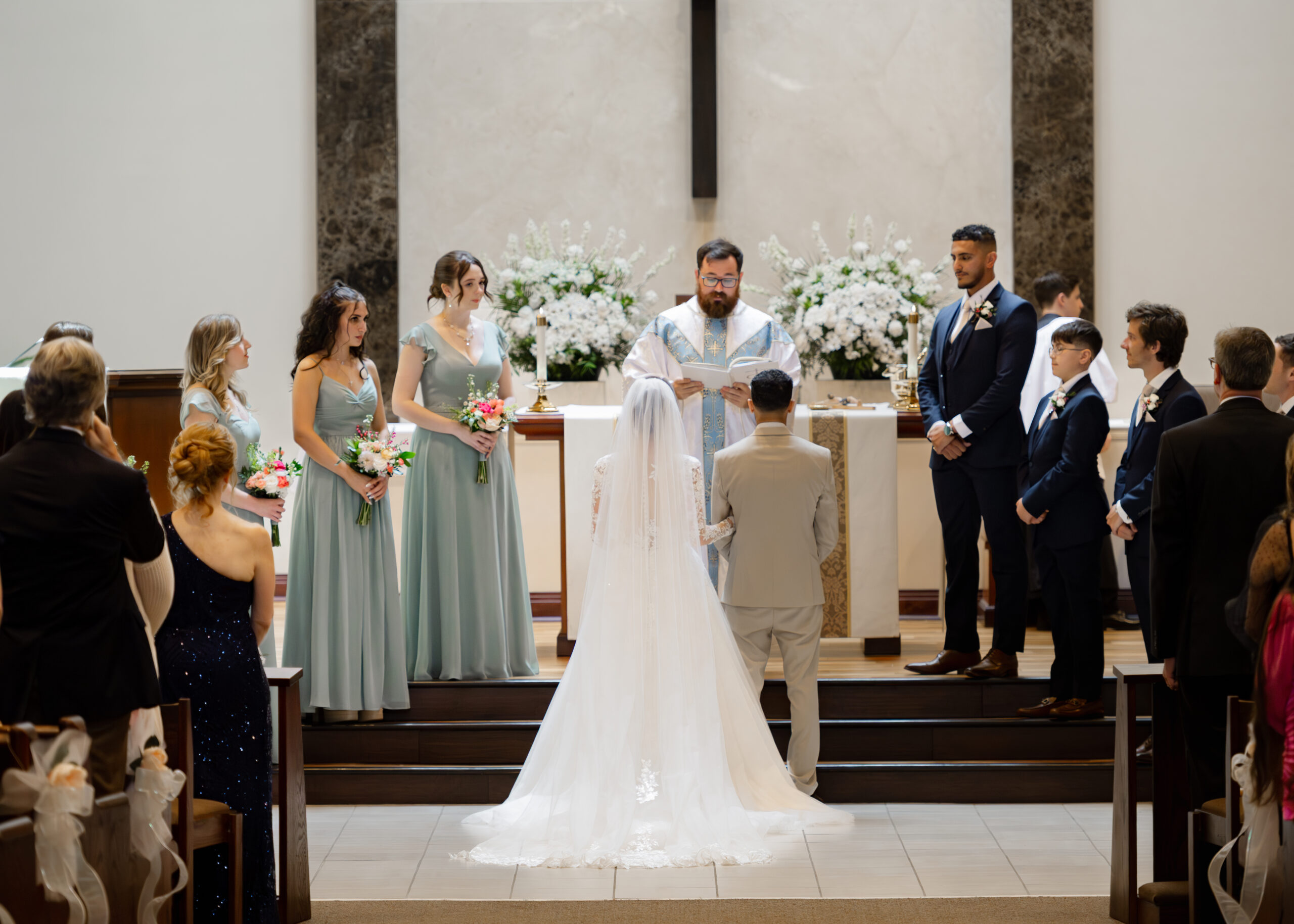 A couple stands at the altar with their bridal party and a priest during a catholic wedding Mass at Holy Family Catholic Church in Brentwood, TN.