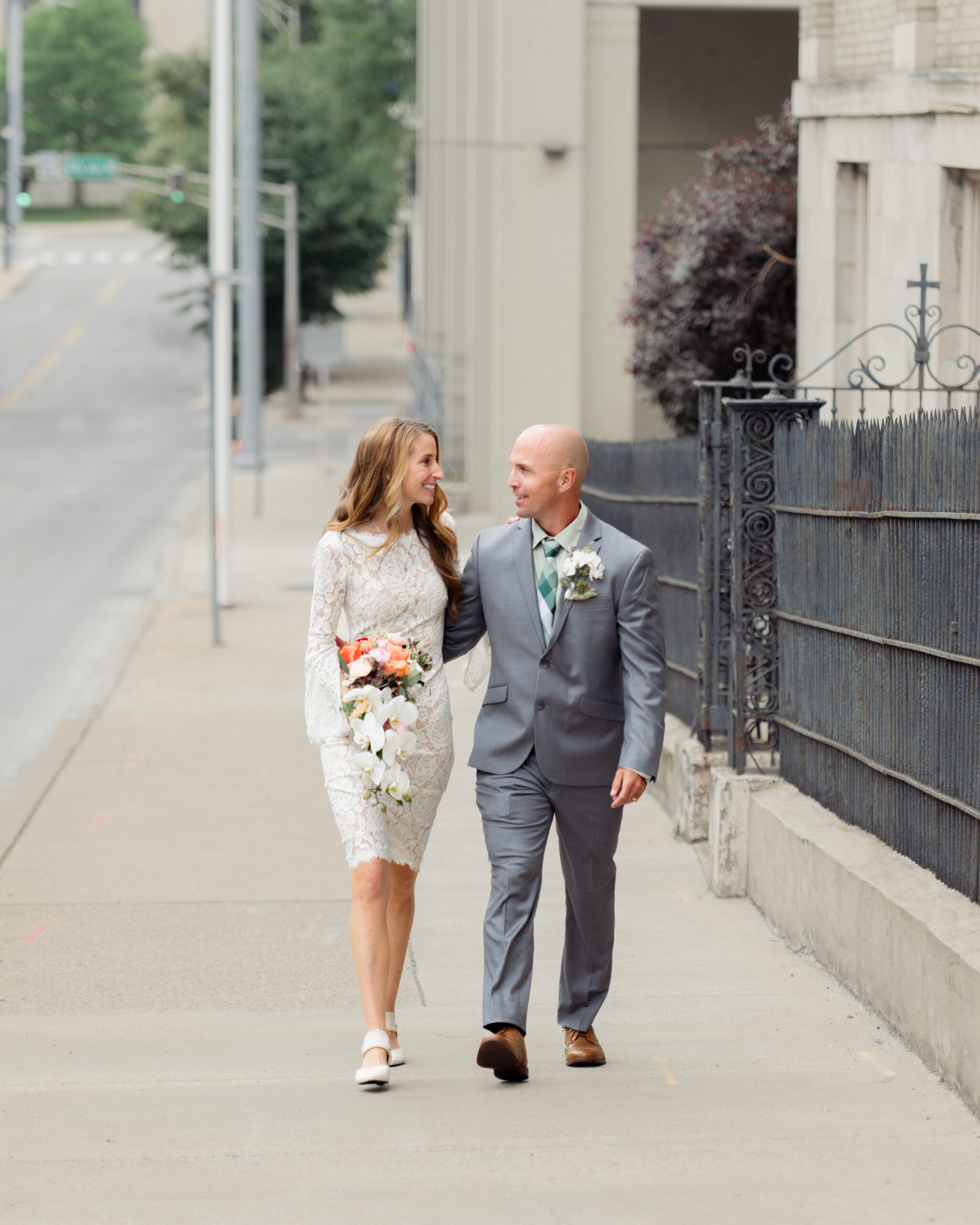 A catholic bride and groom laugh, look at each other, and walk down the sidewalk together outside of St. Mary's in downtown Nashville after their catholic wedding Mass