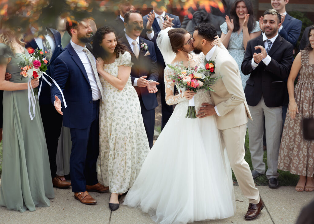a catholic bride and groom kiss as all of their church friends cheer after their catholic wedding mass at holy family catholic church outside of nashville, tn