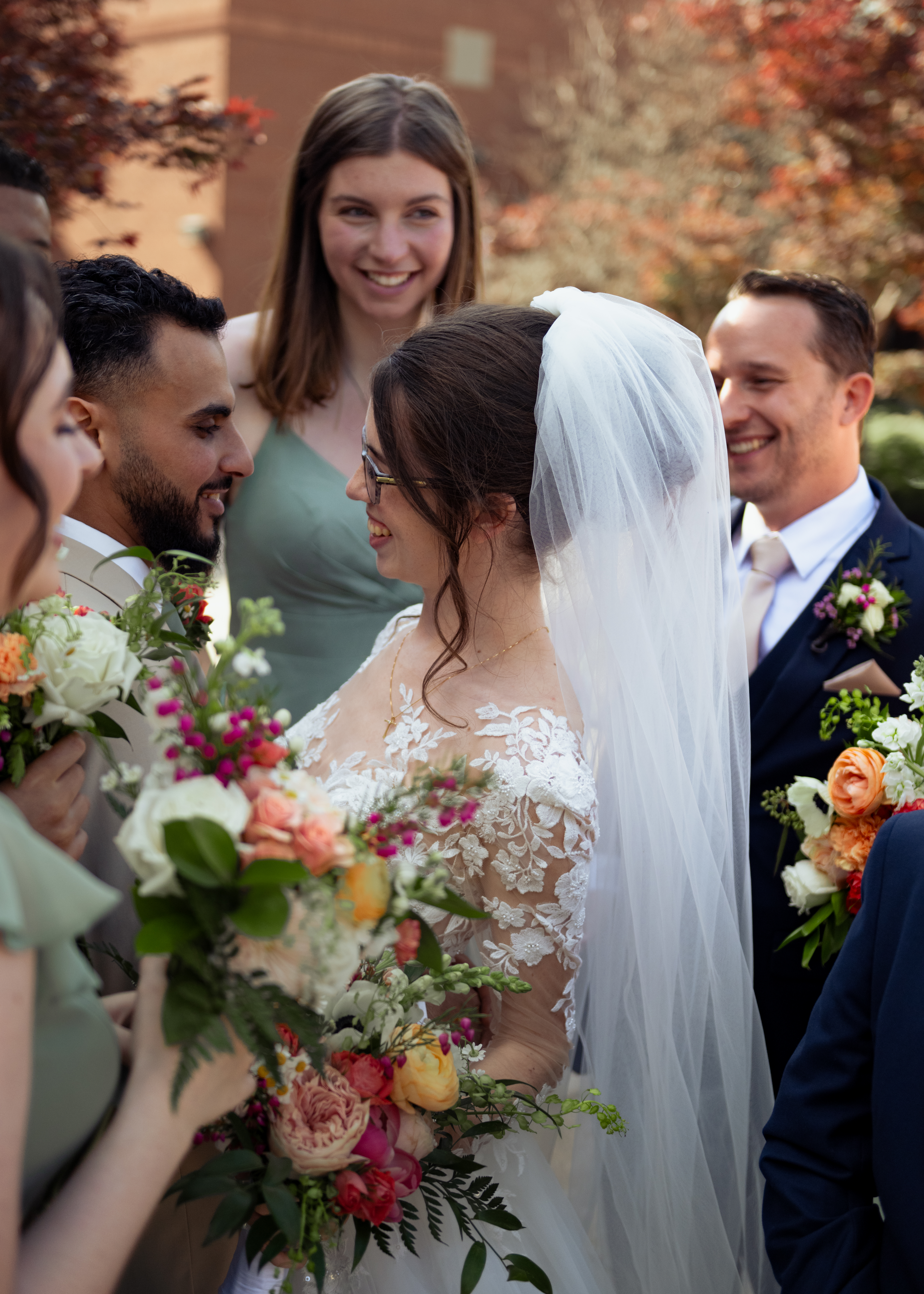 A catholic groom and bride laugh at each other as their friends surround them after their catholic wedding at holy family catholic church in brentwood, tn