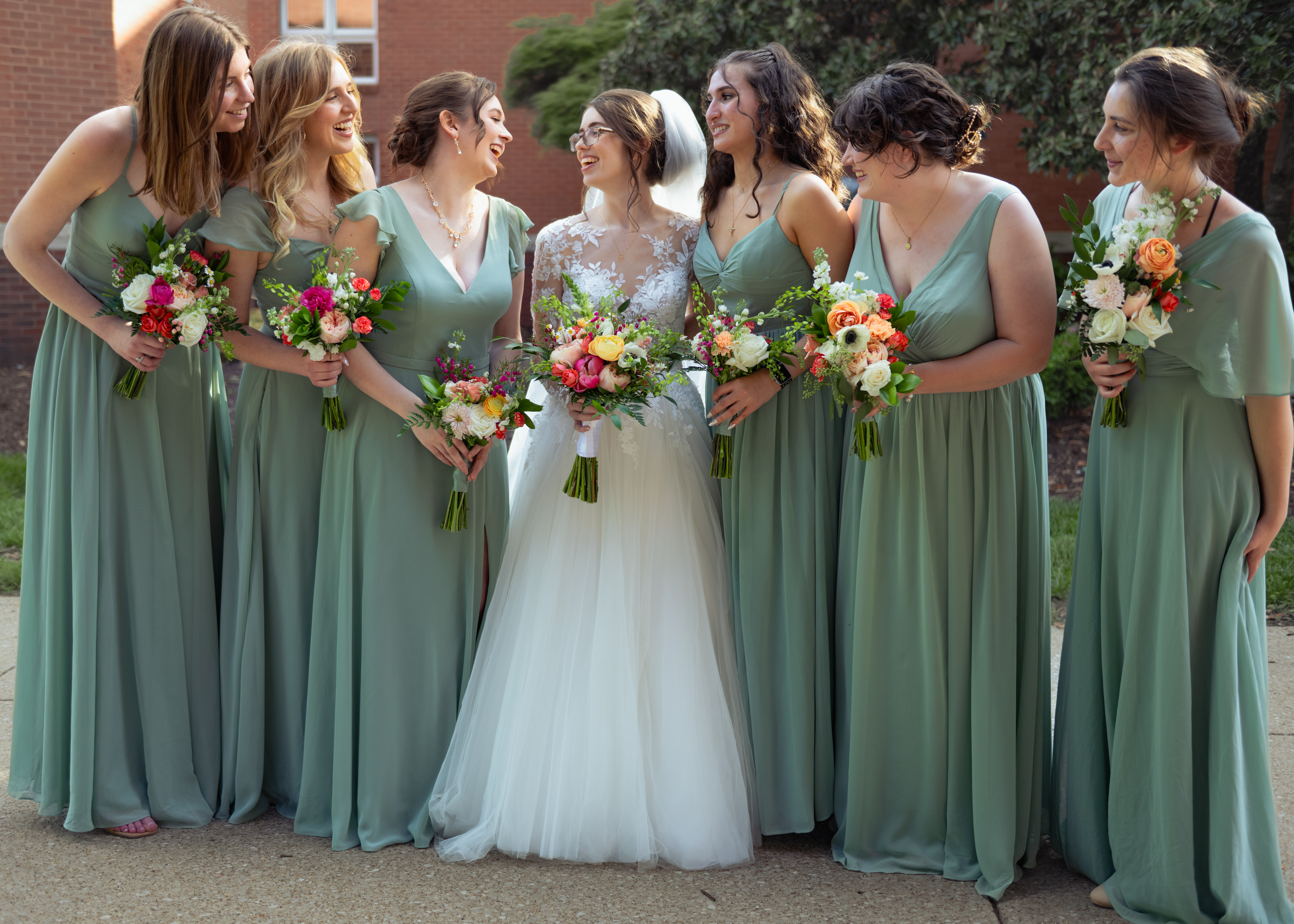 A bride grins at her bridesmaids who surround her after her catholic wedding at holy family catholic church in brentwood, tn