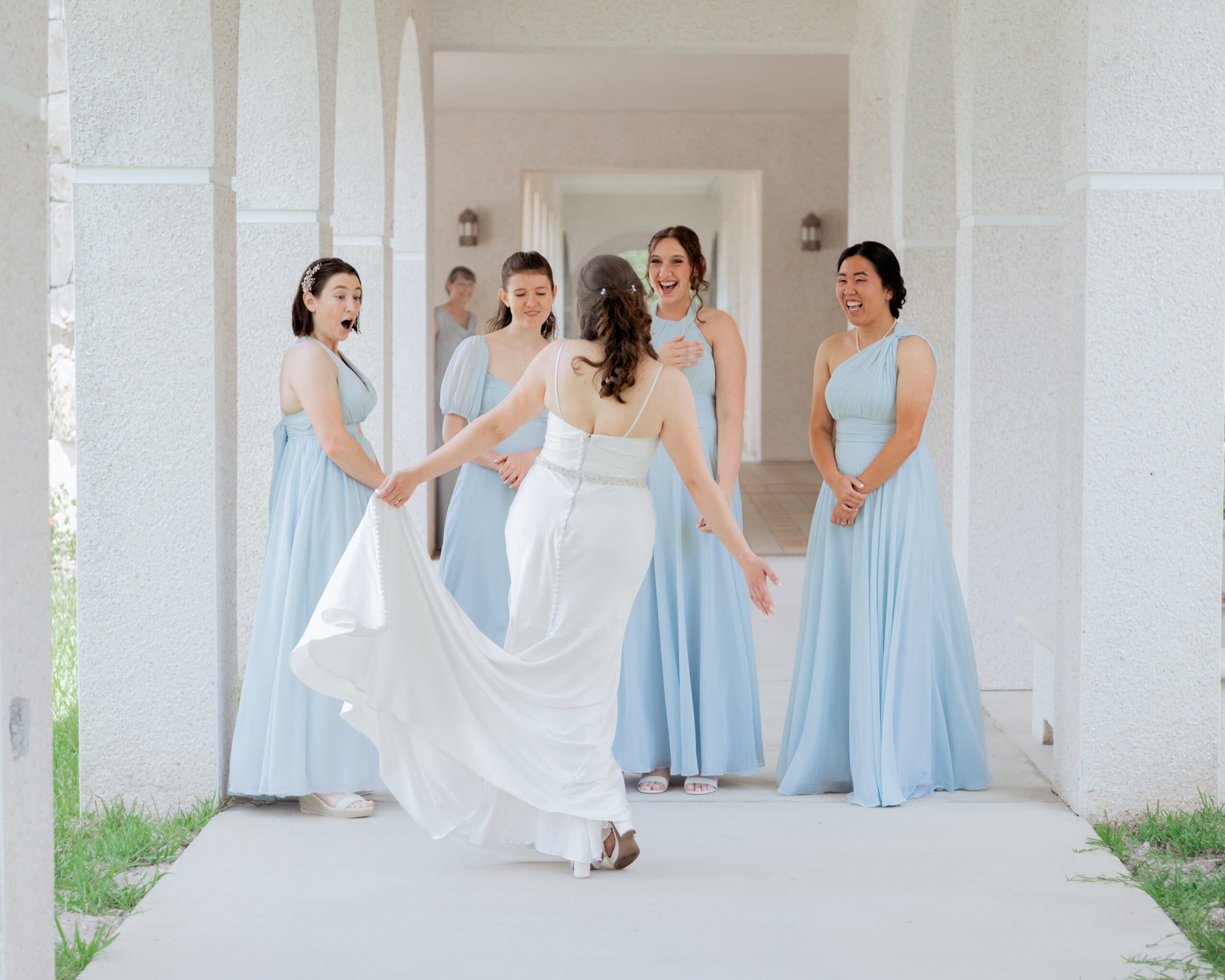A beautiful first look between the bride and her bridesmaids, as the bride spins in her satin gown for the group to see before the Catholic wedding ceremony in St. Augustine, Florida. The bridesmaids’ expressions of surprise and joy reflect the deep bond between them on this special day.
