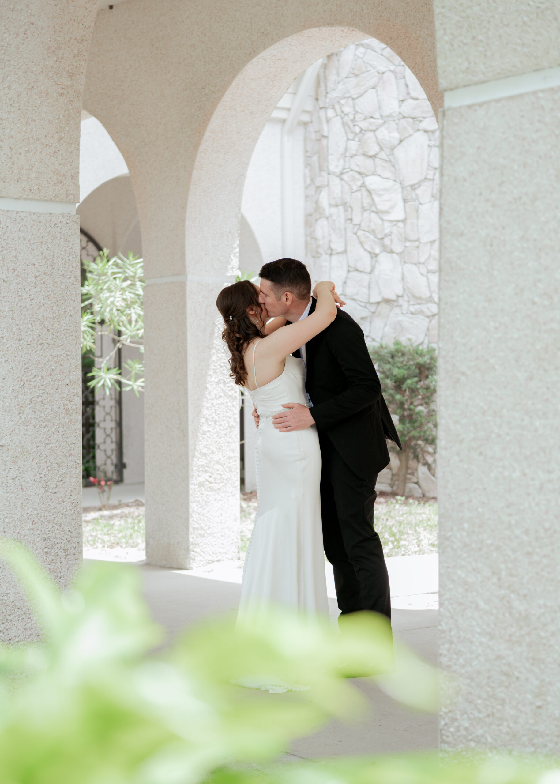 Catholic bride and groom sharing a kiss under the stone archways at St. Anastasia’s Catholic Church before their sacred wedding vows.
