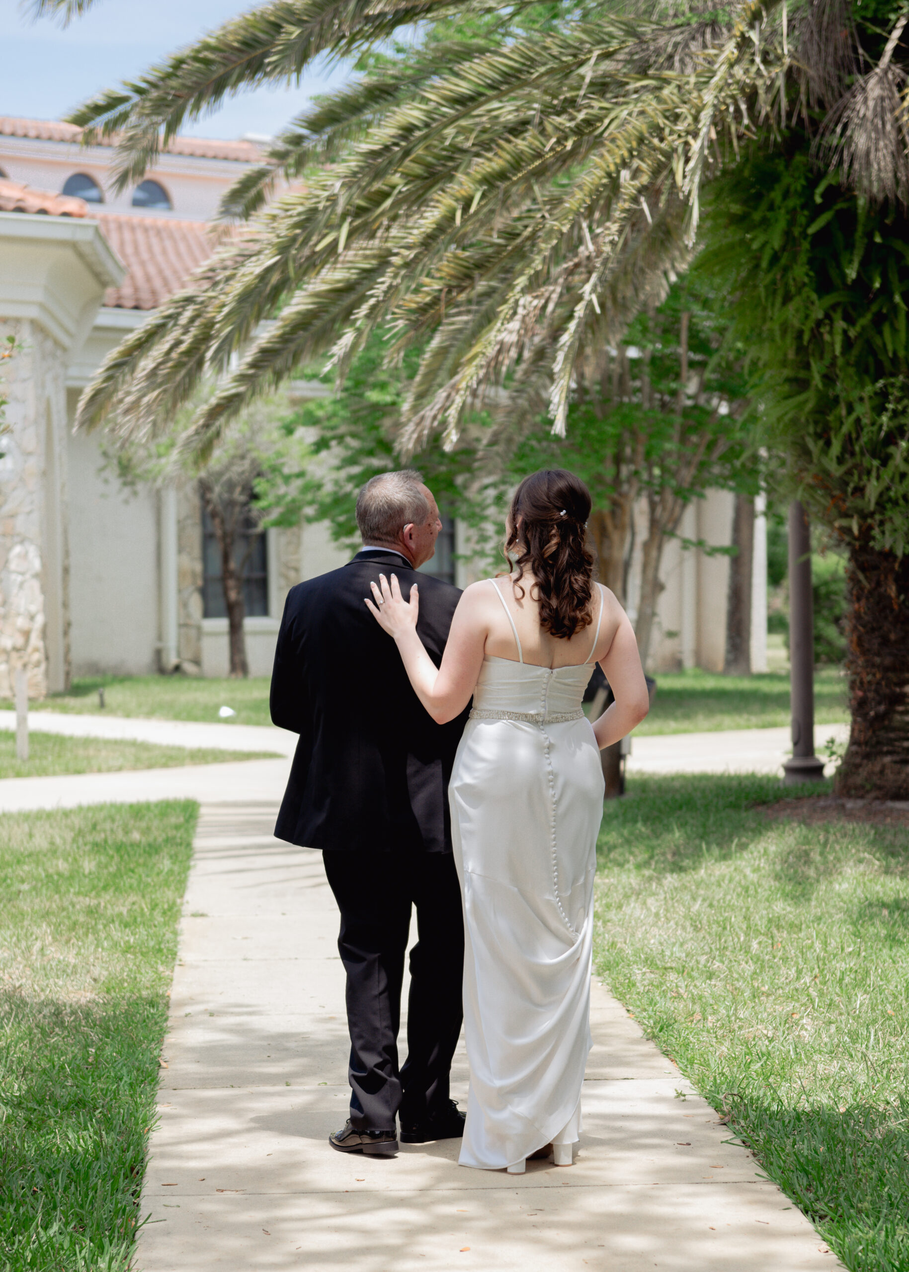 A touching first look between the bride and her father before the Catholic wedding in St. Augustine, Florida. The father, dressed in a black tuxedo, looks on proudly as his daughter, in her beautiful satin wedding gown, smiles at him, capturing a moment of love and emotional connection.