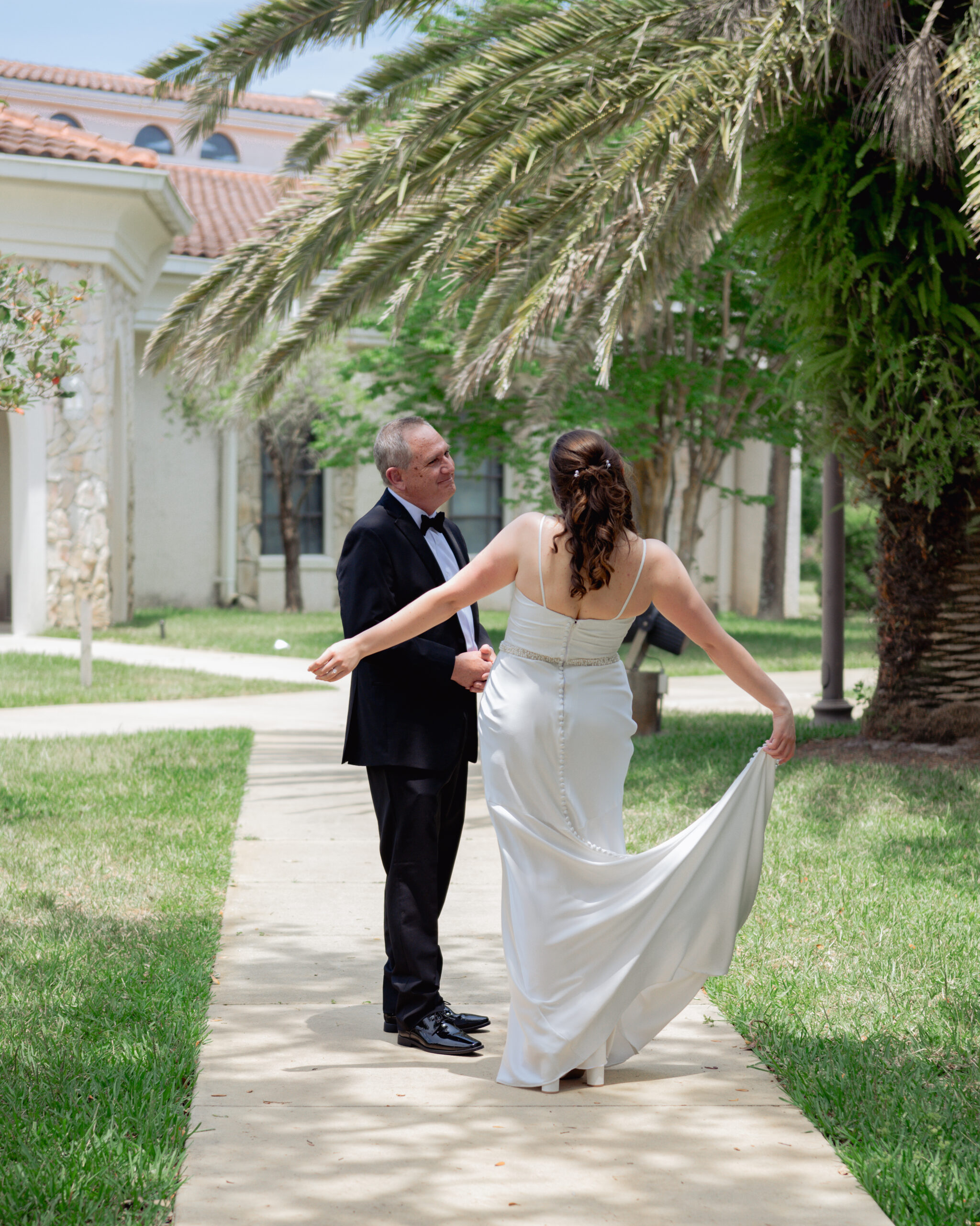 The bride and her father share an emotional first look before walking down the aisle at a Catholic wedding in St. Augustine, Florida. The bride, in her satin gown, spins gracefully for her father, who beams with pride, capturing the love and bond between them ahead of the ceremony.