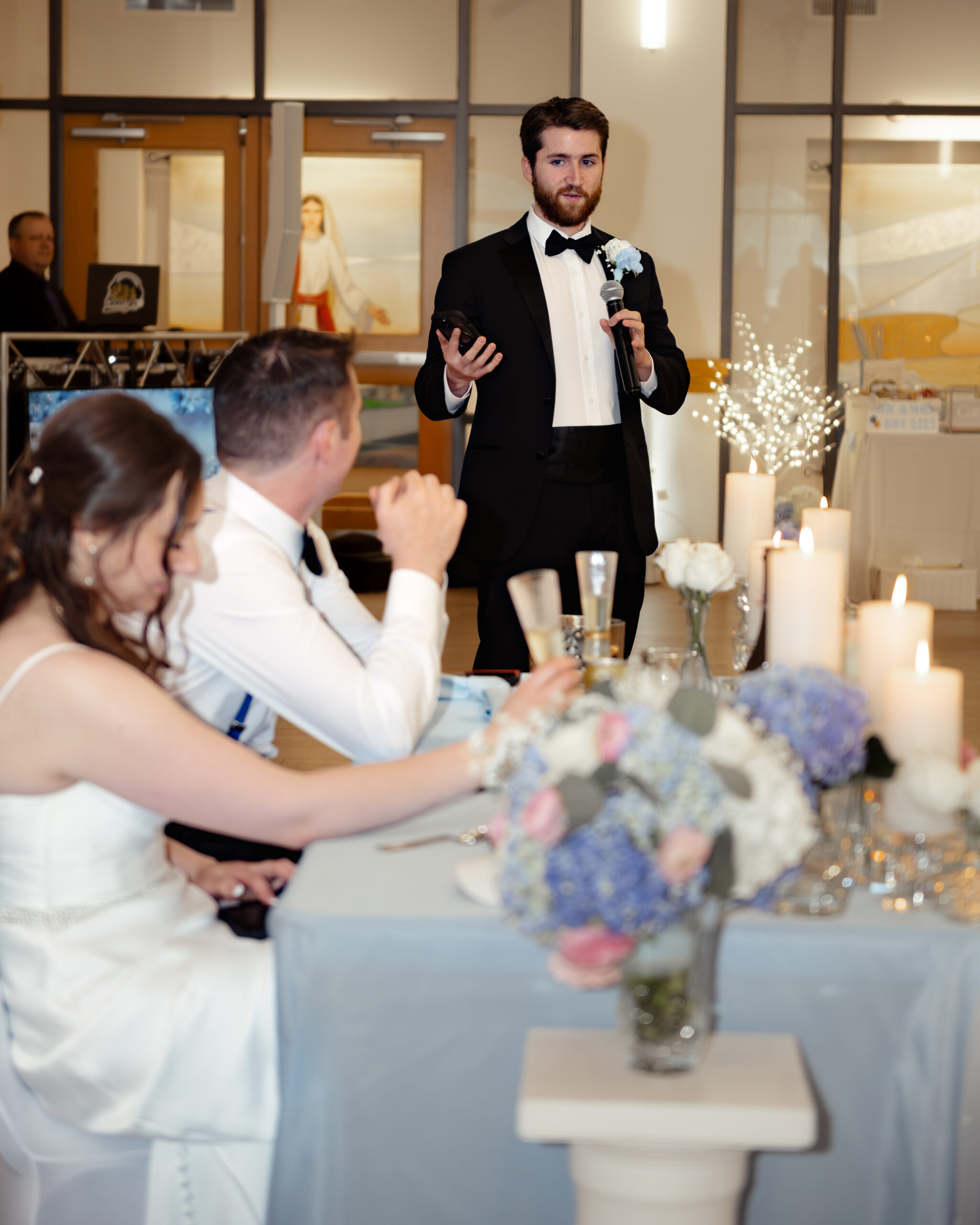 Best man delivers a heartfelt wedding toast to the bride and groom during their reception at St. Anastasia Catholic Church in St. Augustine. Elegant white candles and floral centerpieces decorate the sweetheart table.