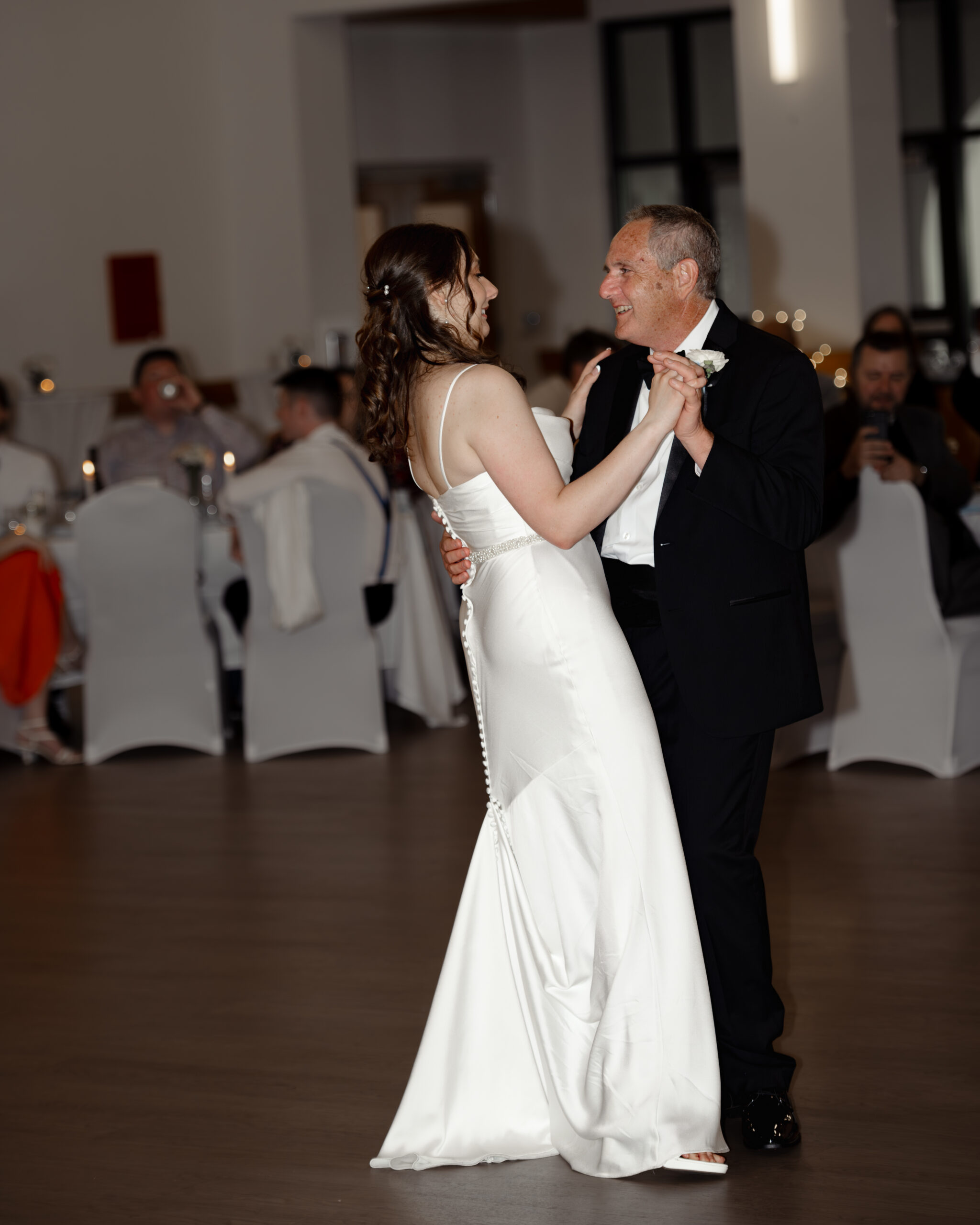 Bride dances with her father in a touching father-daughter dance at the St. Anastasia Catholic Church wedding reception in St. Augustine. The bride’s elegant white gown flows gracefully as they smile together.
