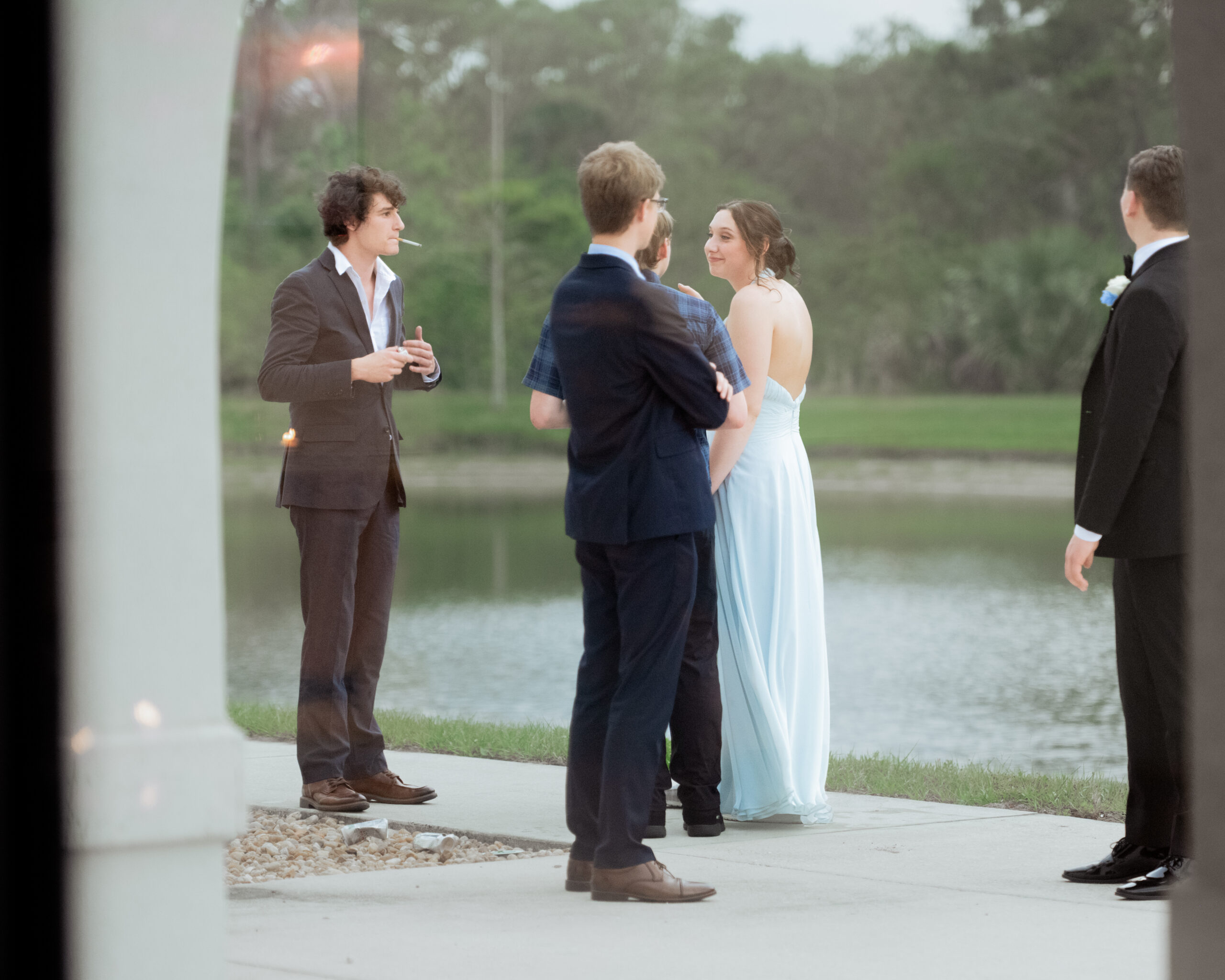 Wedding guests in formal attire socialize beside the scenic lake outside St. Anastasia Catholic Church during a Catholic wedding reception in St. Augustine, Florida.