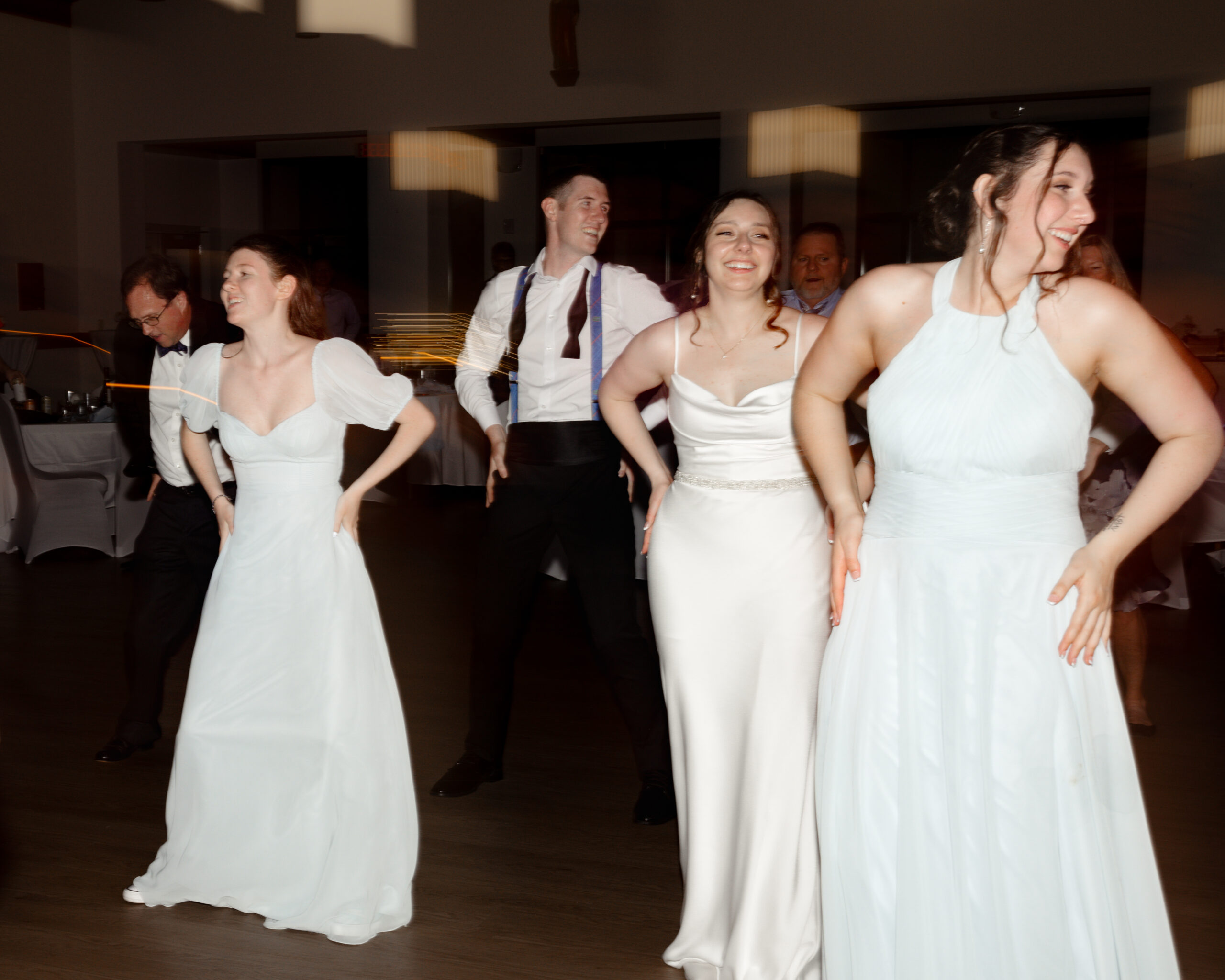 Bride and bridesmaids wearing elegant gowns joyfully dancing during a Catholic wedding reception at St. Anastasia Catholic Church in St. Augustine, Florida.