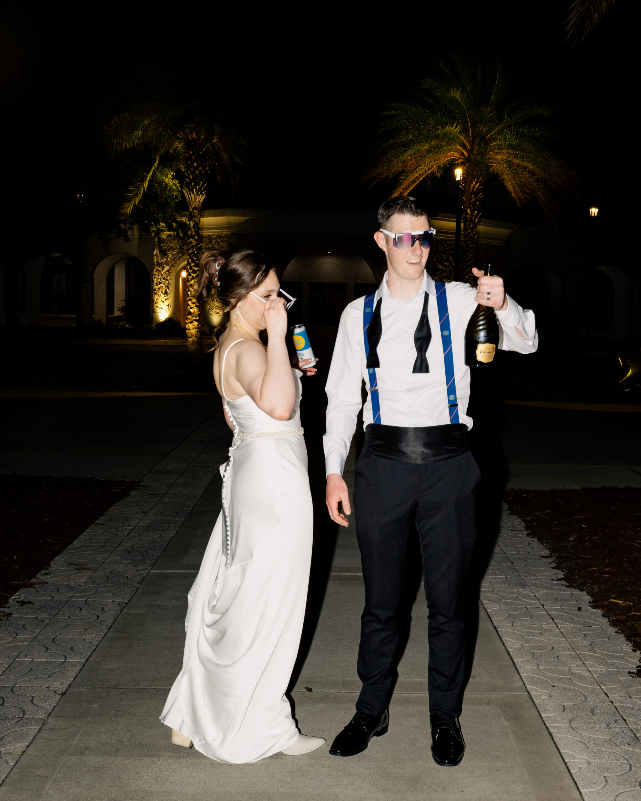 Bride and groom enjoying their Catholic wedding reception, holding drinks and wearing fun sunglasses outside St. Anastasia Catholic Church in St. Augustine, FL.