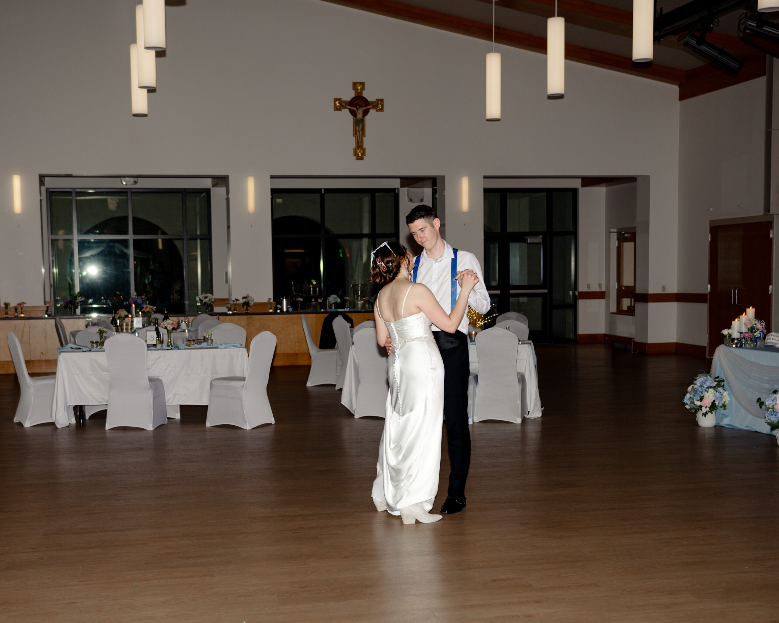 The bride, in her wedding dress, dances closely with a groomsman wearing navy suspenders during a Catholic wedding reception in a decorated church event hall at st. anastasia catholic church in st. augustine, florida