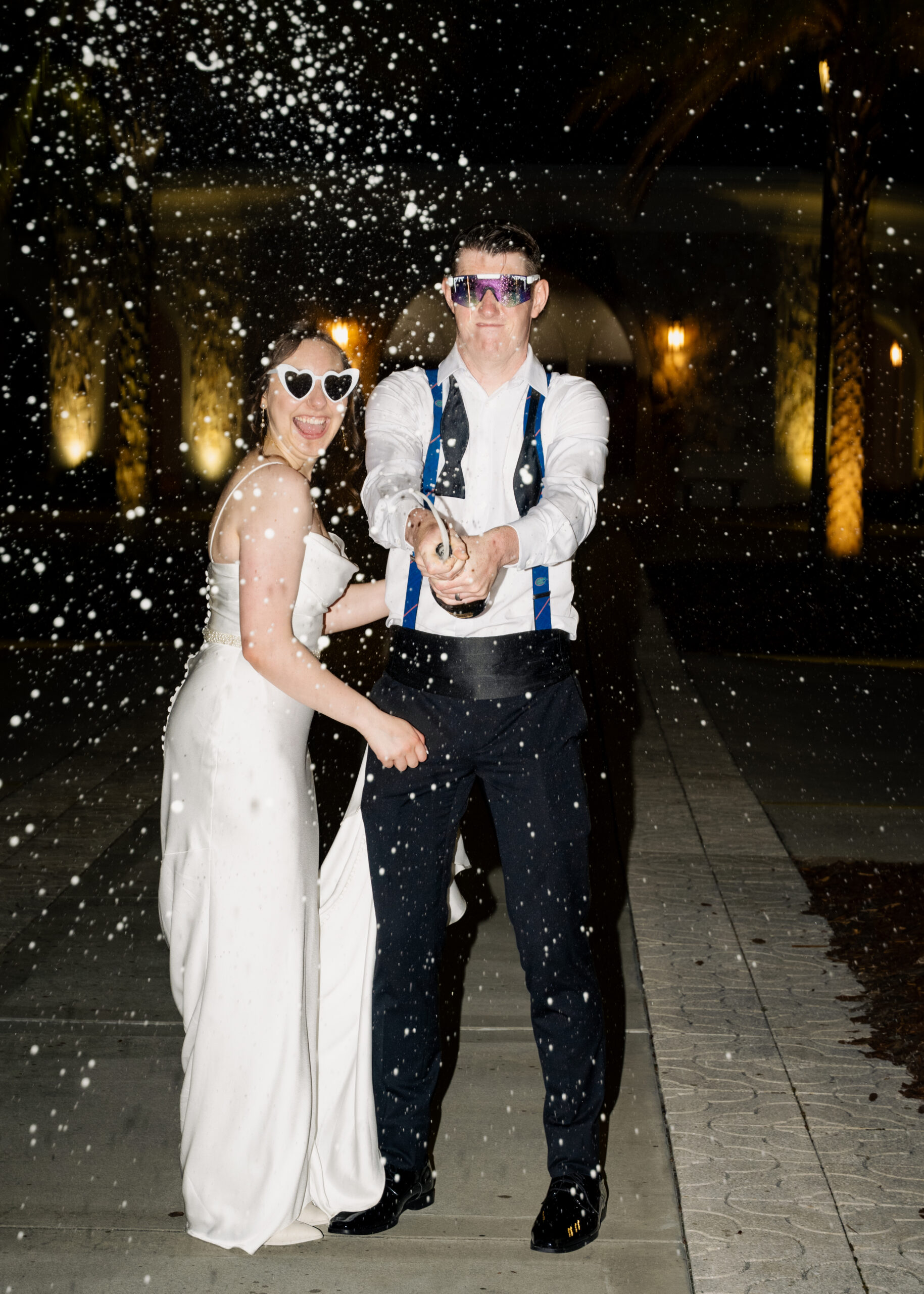champagne sprays as the bride and groom celebrate their Catholic wedding outside St. Anastasia Catholic Church in St. Augustine, Florida, captured in a fun nighttime photo.
