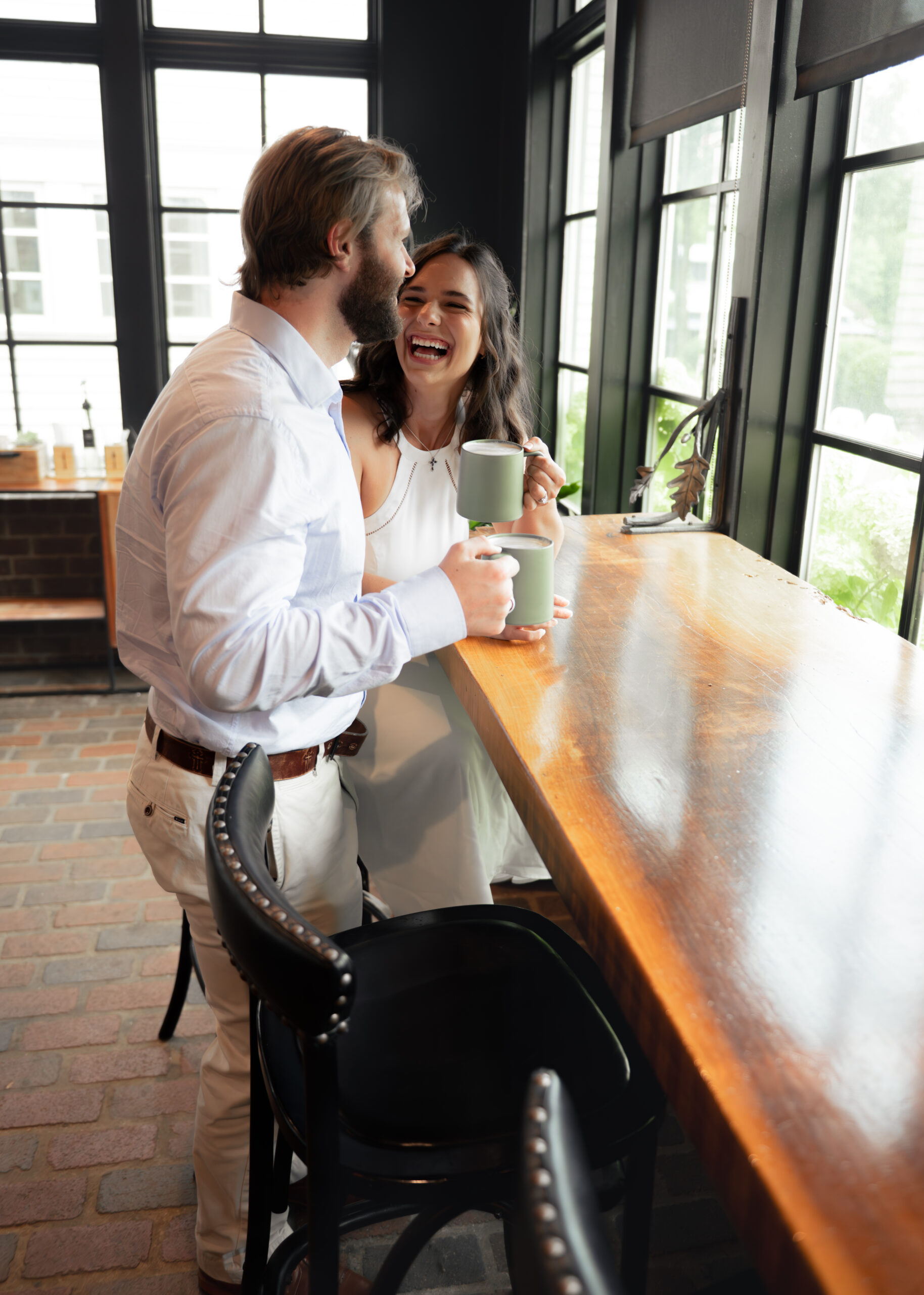 A wide shot of a catholic couple laughing together during their relaxed engagement session at a coffee shop in Thompson's station, tn