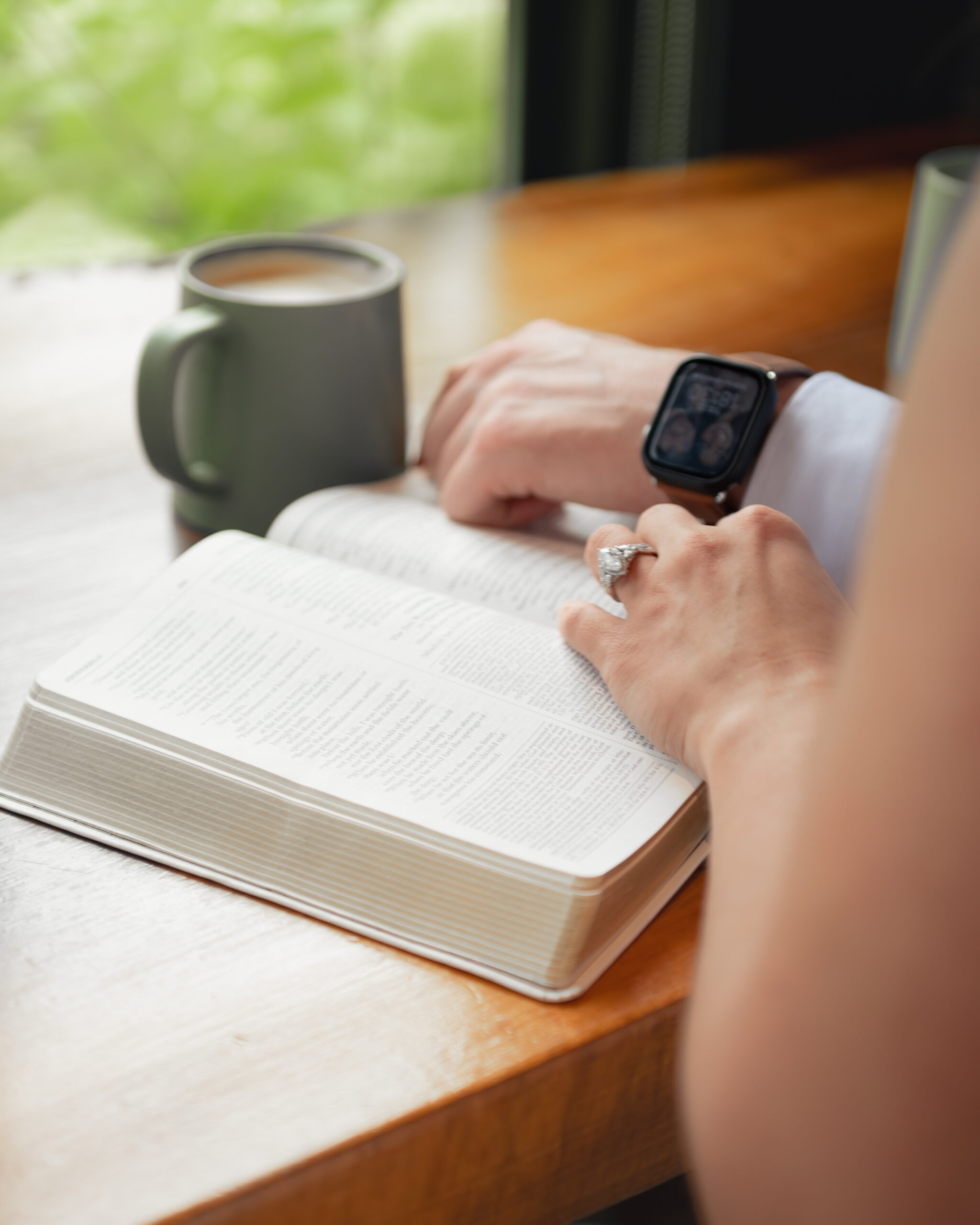 a detail photograph shows a coffee cup, a bible, a female hand wearing an engagement ring, and a male wrist wearing an apple watch with a portrait