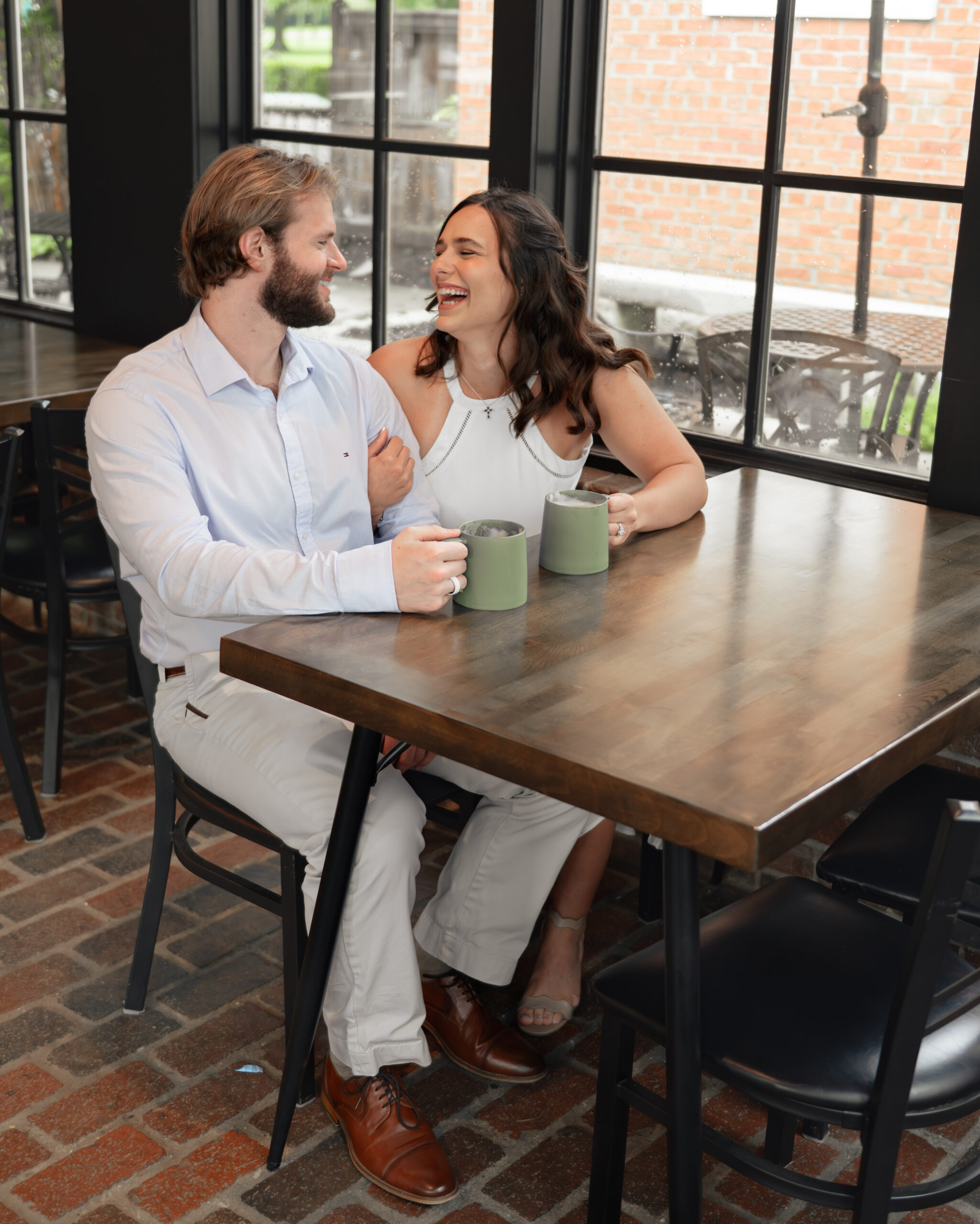 A catholic couple laughs together during a joyful moment during their coffee shop engagement session in thompson's station, tn
