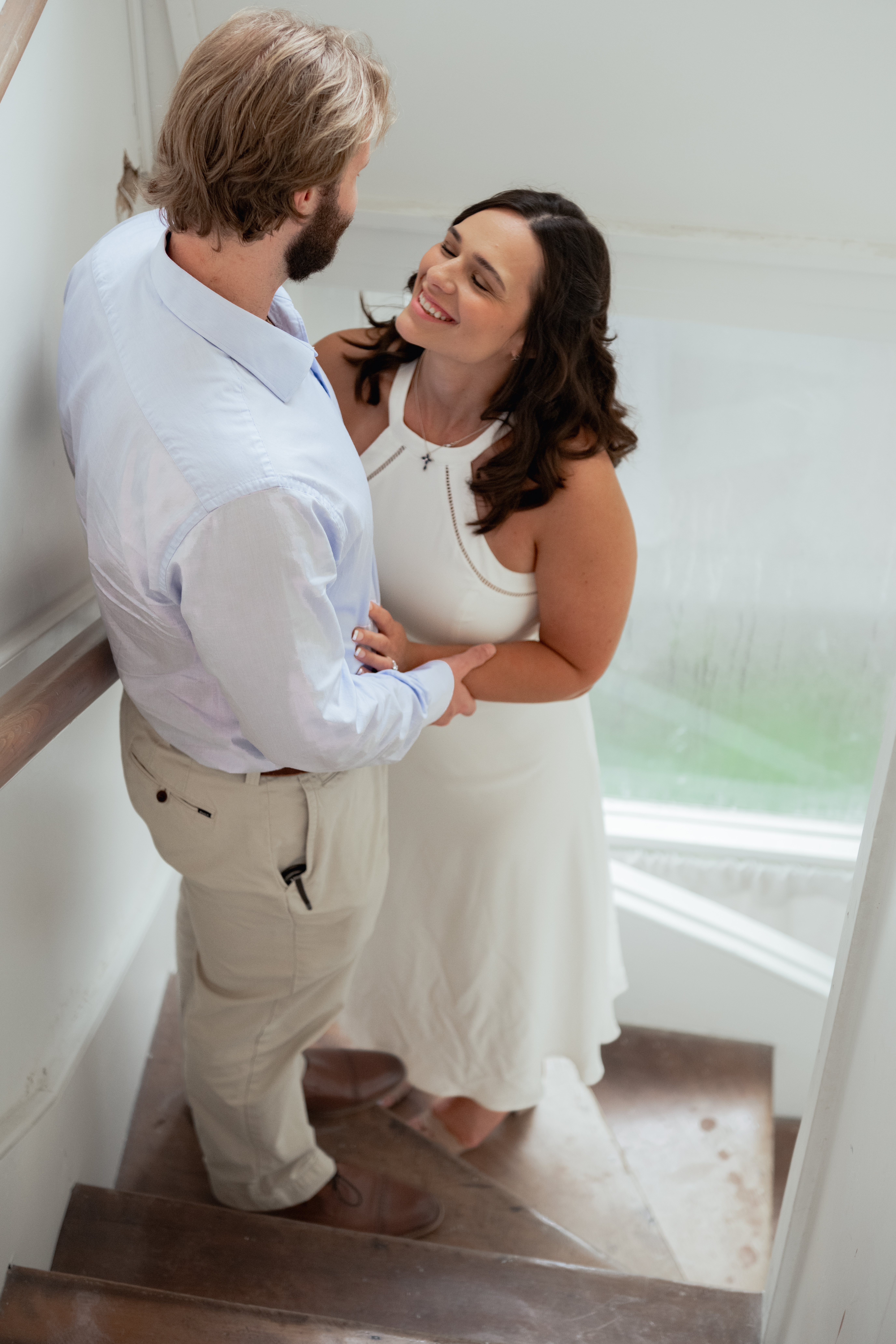 A catholic couple smiles as they hold hands in a hazy but bright back staircase of a historic mansion in thompson's station, tn