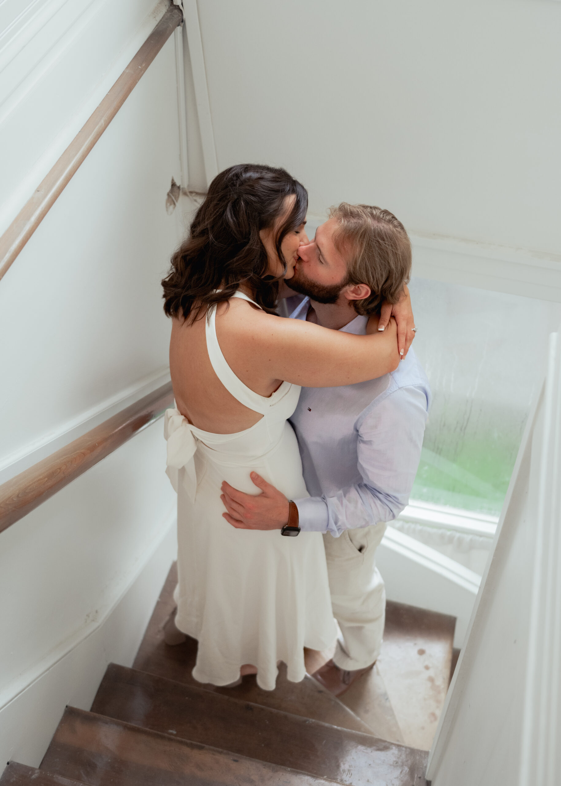 A catholic bride and groom kiss in a bright staircase of a tennessee mansion during their engagement session