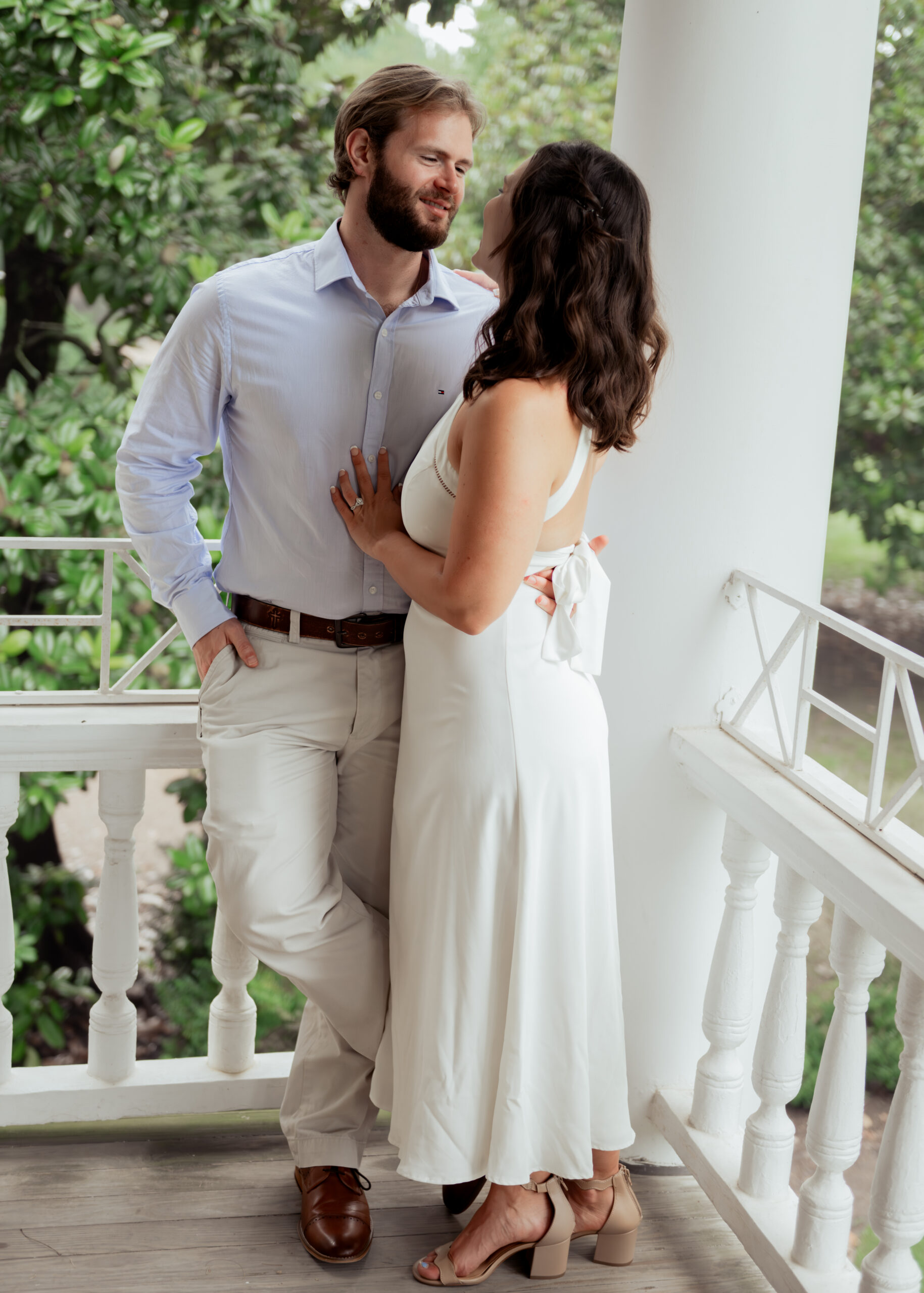A catholic groom romantically pulls his bride closer on the front balcony of a historic tennessee mansion during their engagement session