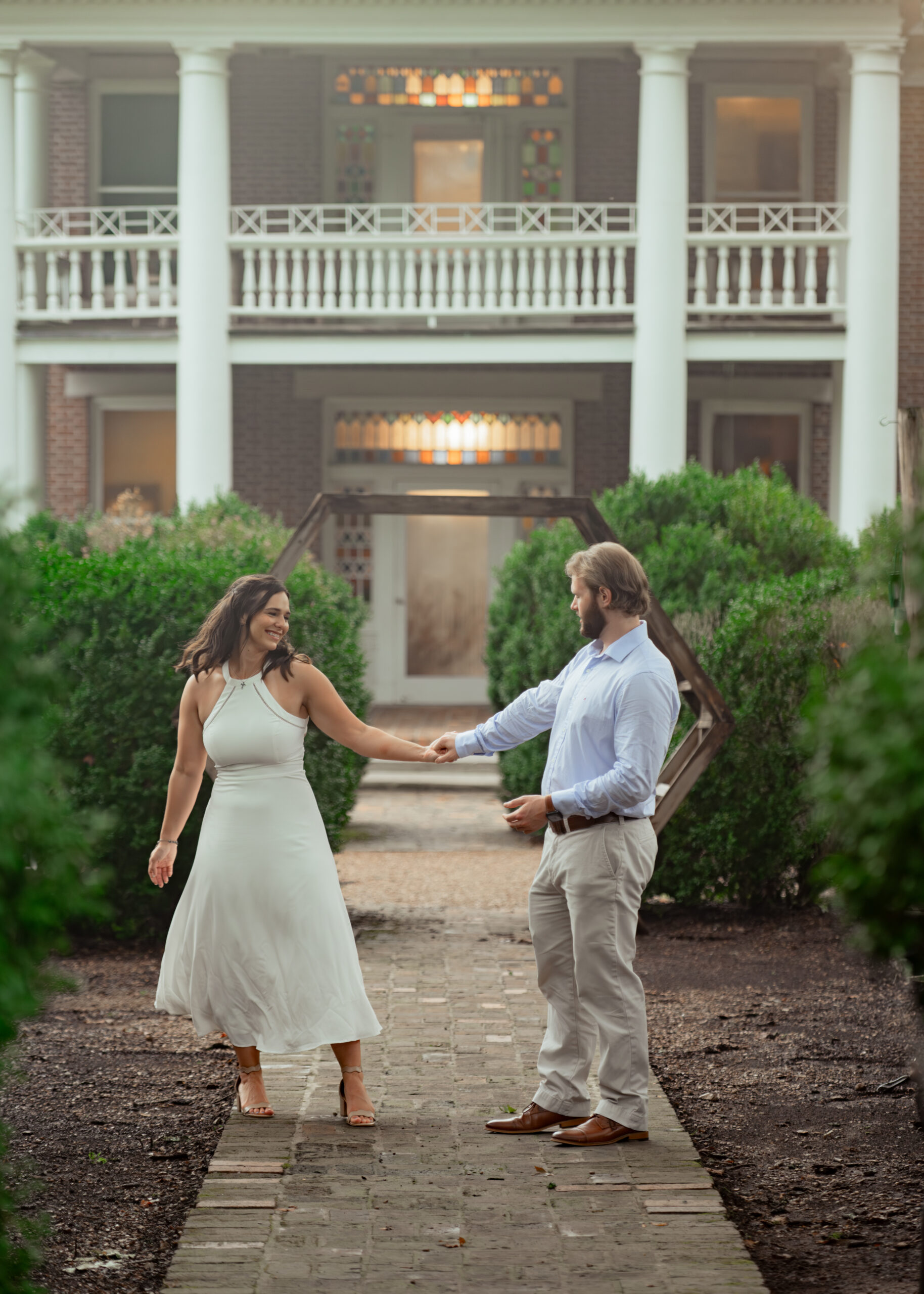 A catholic couple dances in front of a historic mansion with hazy light in this loose editorial engagement session portrait