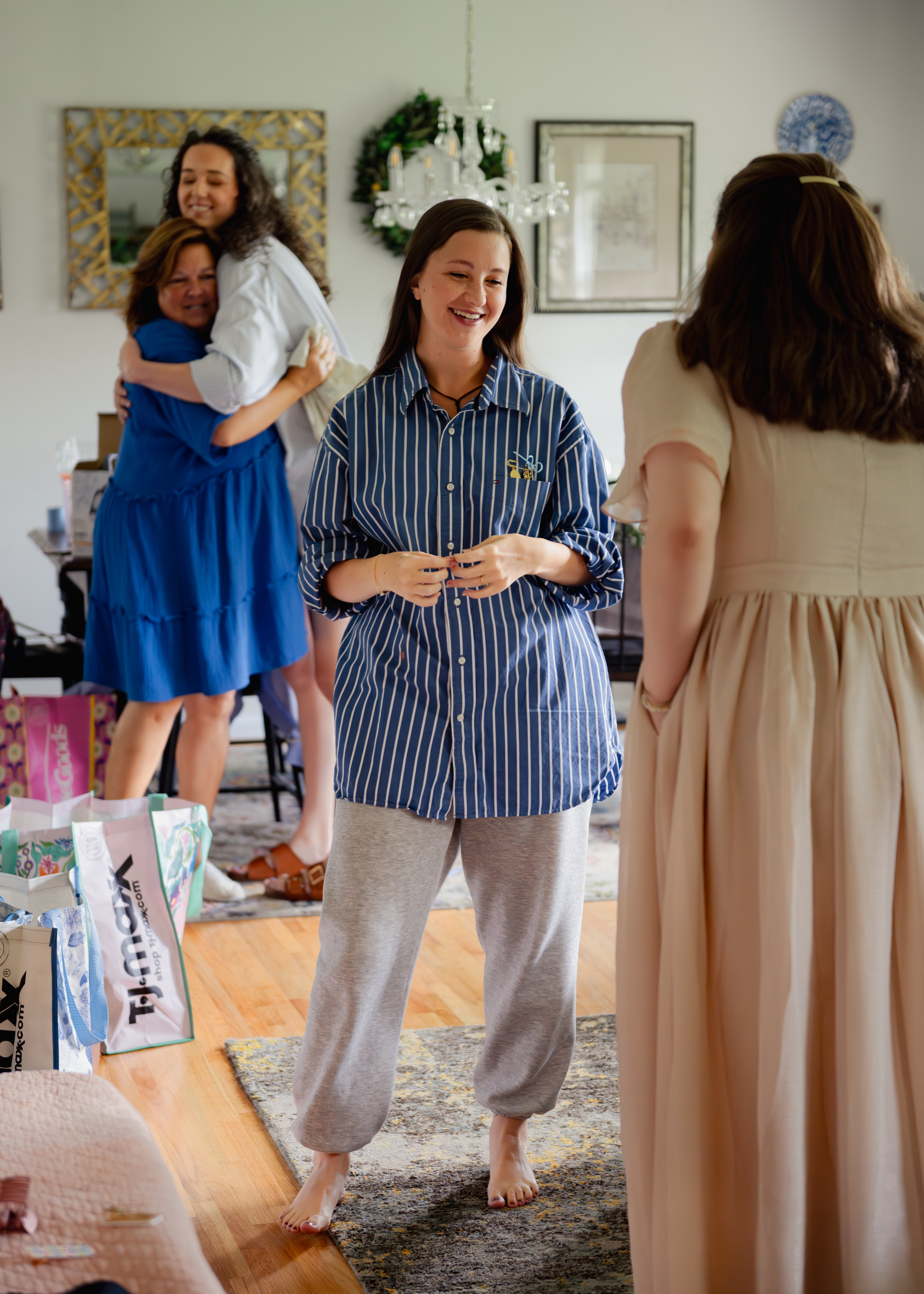 Bridesmaids laugh as they get ready in the bride's living room while the bride hugs a friend in the background in this documentary wedding getting ready photograph