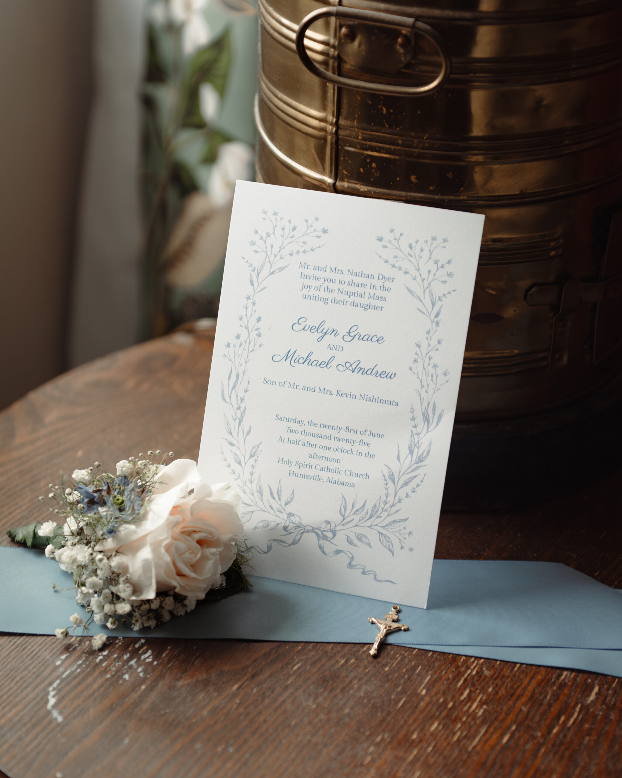an environmental details photograph shows the relaxed and catholic nature of this wedding and the invitation, a crucifix, and a boutenniere.