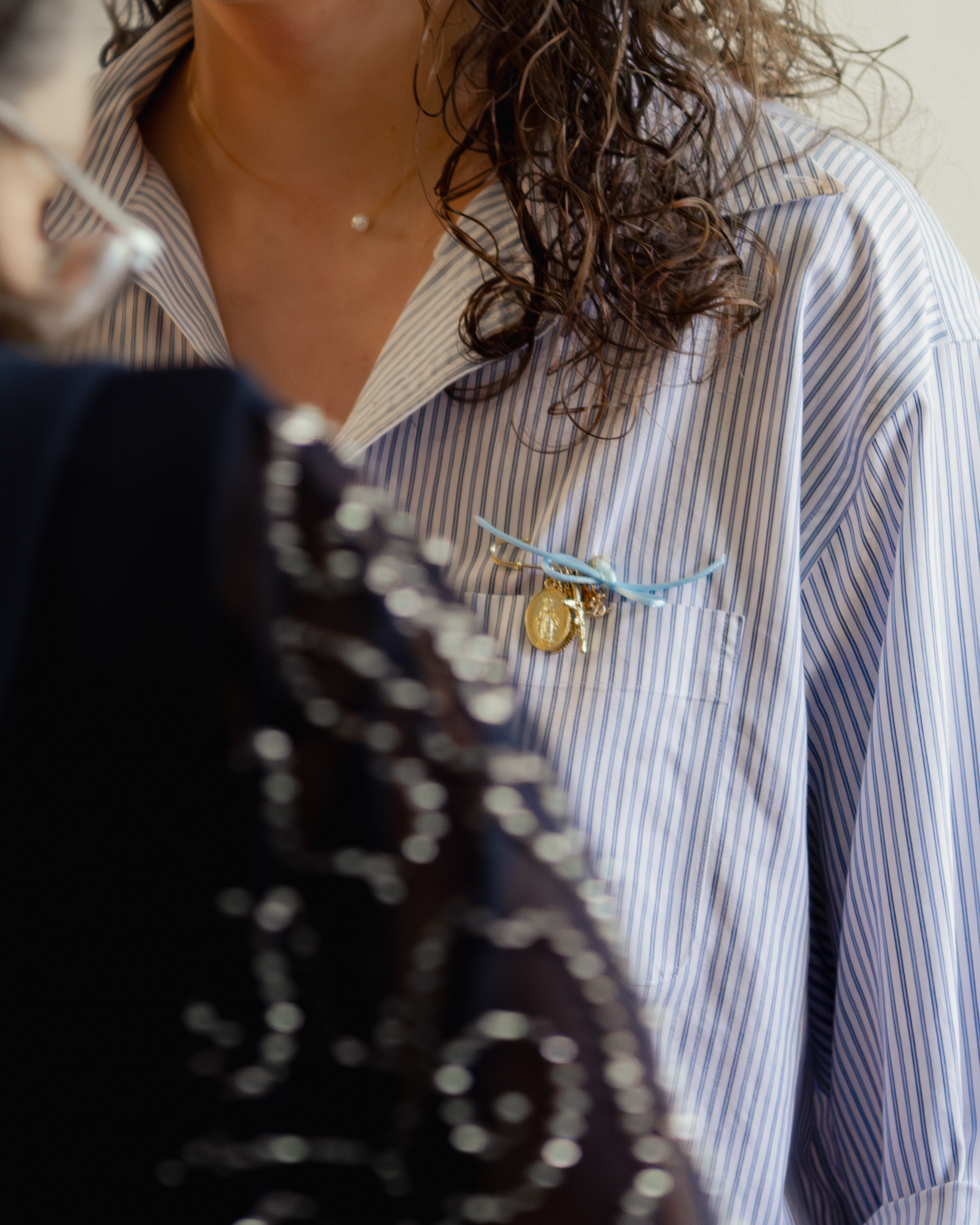 a detail photograph shows the bride wearing a pin with her favorite catholic saint medals as a way she is intentionally incorporating her catholic faith into her wedding day.