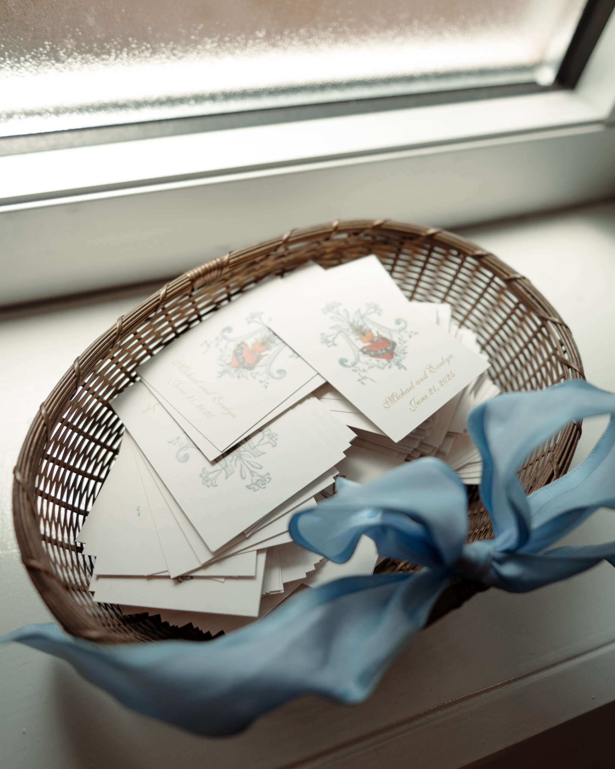 a basket on a windowsill holds a pile of prayer cards as favors from a catholic bride and groom to their guests as a way they intentionally incorporated their faith into their catholic wedding day.