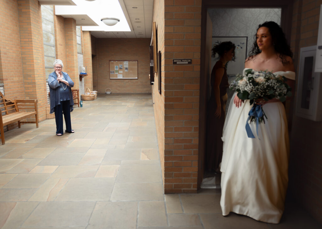 A bride comes around the corner of a catholic church after putting on her wedding dress to surprise her grandmother